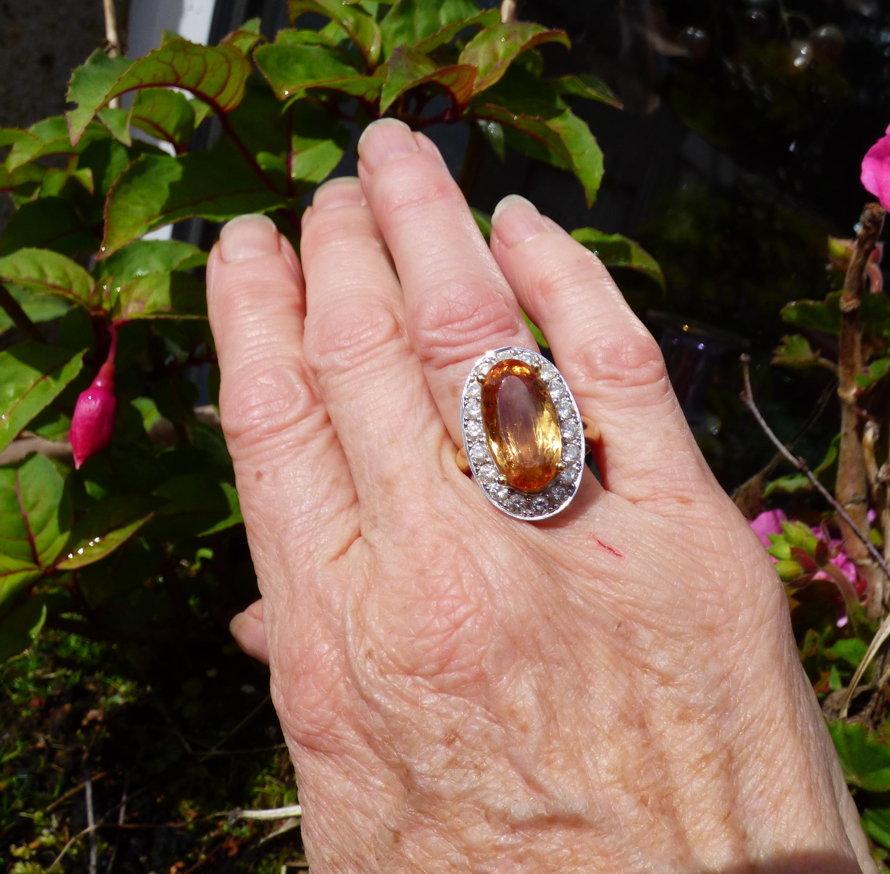 This ring fills the finger like no other! The bright colourful Imperial Topaz is 18X9mm in size weighing 10.3ct.  The claw set Topaz is surrounded by 18 Diamonds with a total Diamond weight of 1.46ct. The ring is handmade in 18K yellow gold with the