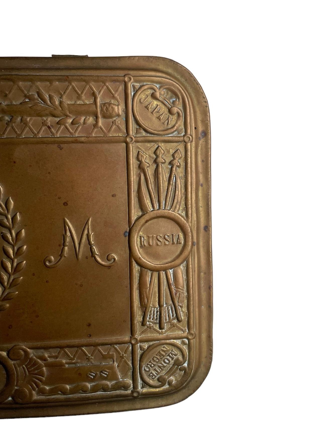 This is an Imperium Britannicum Christmas, 1914 bronze color brass tin tobacco box. The hinged lid of the box depicts a profile of Princess Mary framed with some bay leaves wreath. In the border of the lid, along this decoration are embossed Great