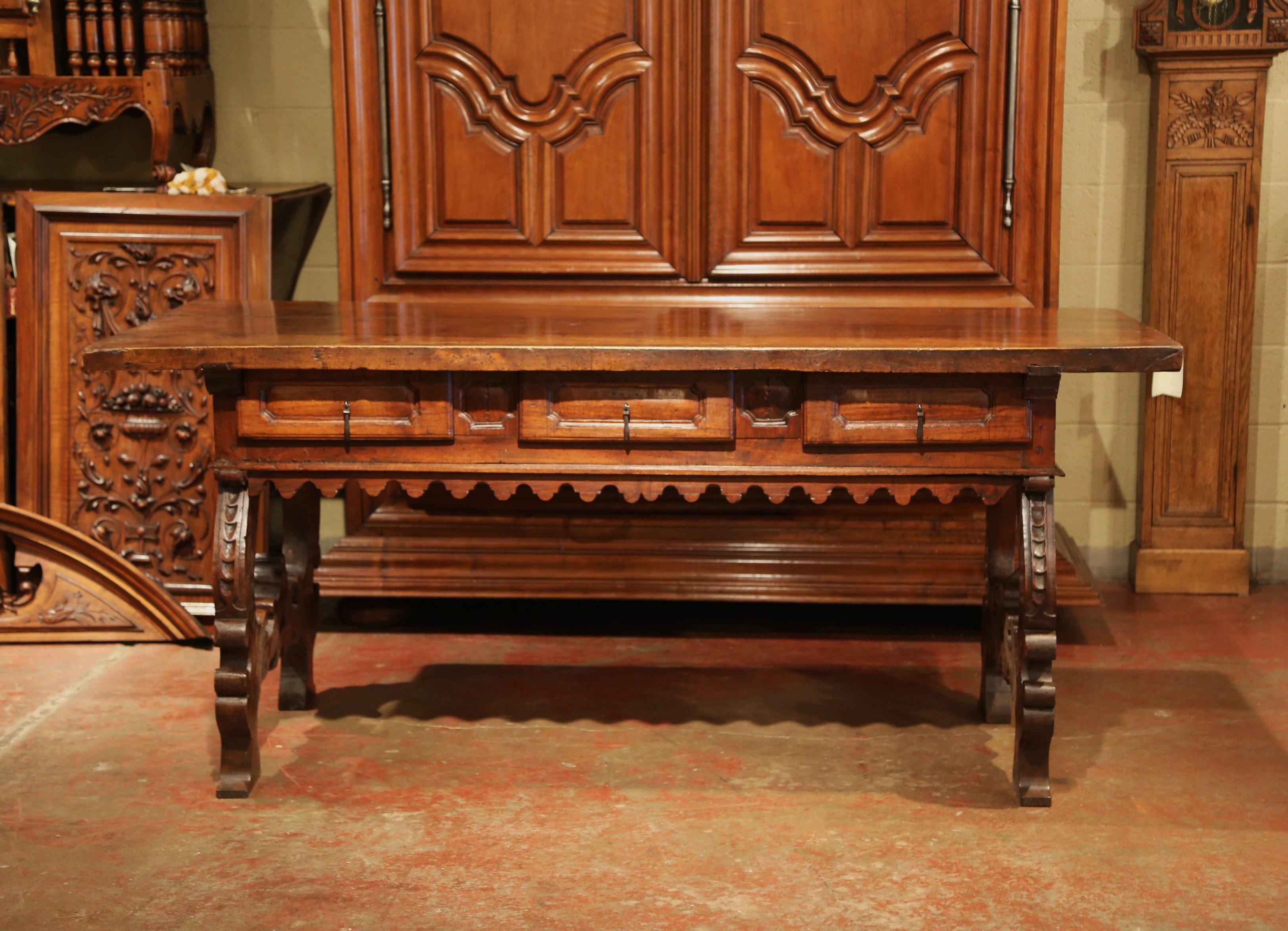 Carved in Spain, circa 1730, this important antique console table flaunts an impressive Gothic style. The large, fruitwood desk top made of a single wooden plank, features three sturdy drawers across the front with original forged pull handles, and