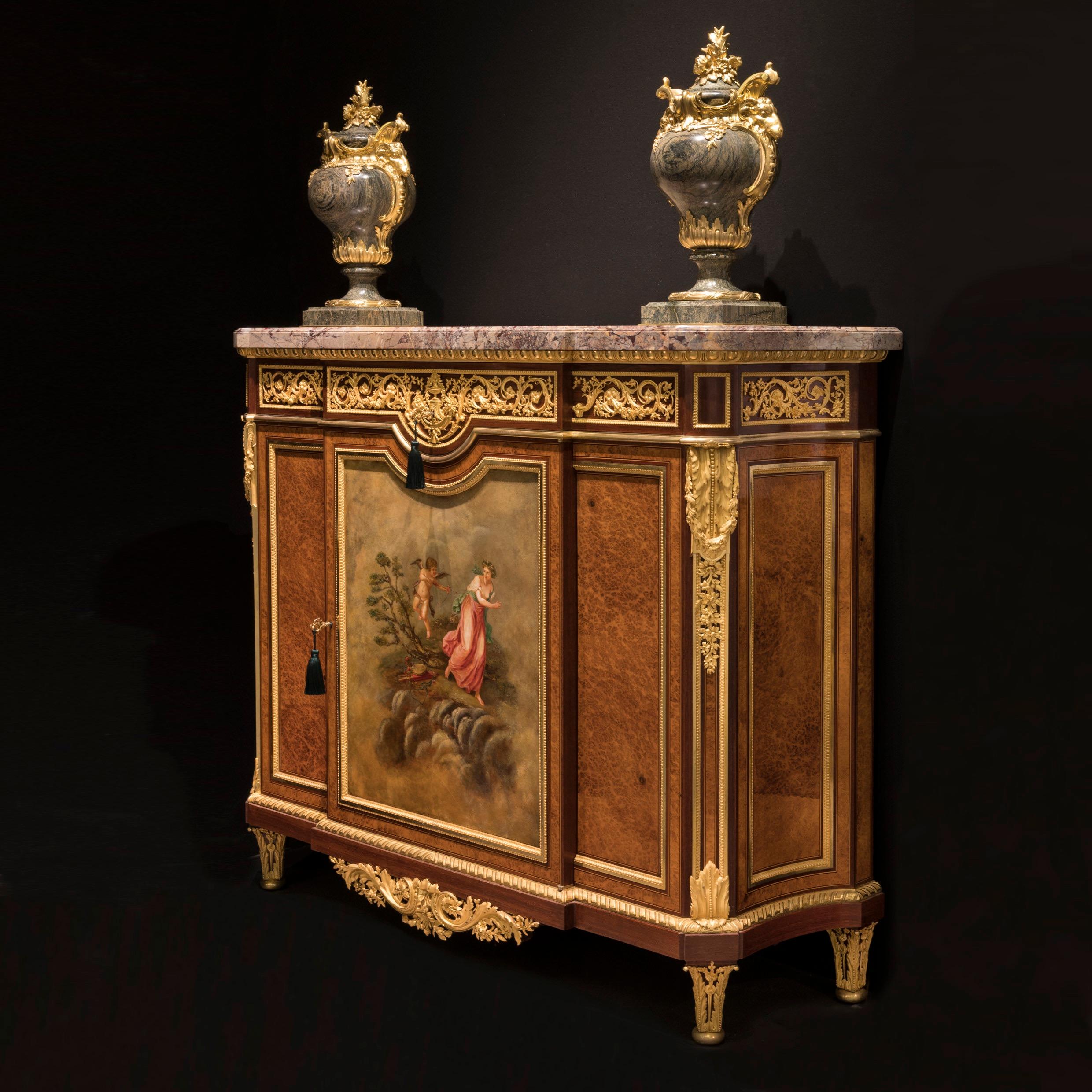 An important side cabinet
By Henry Dasson

Constructed in amboyna and purpleheart, with ebony and boxwood stringing, dressed with fine ormolu mounts. Rising from tapering and bronze collared block feet, the lower apron has a strong gilt bronze