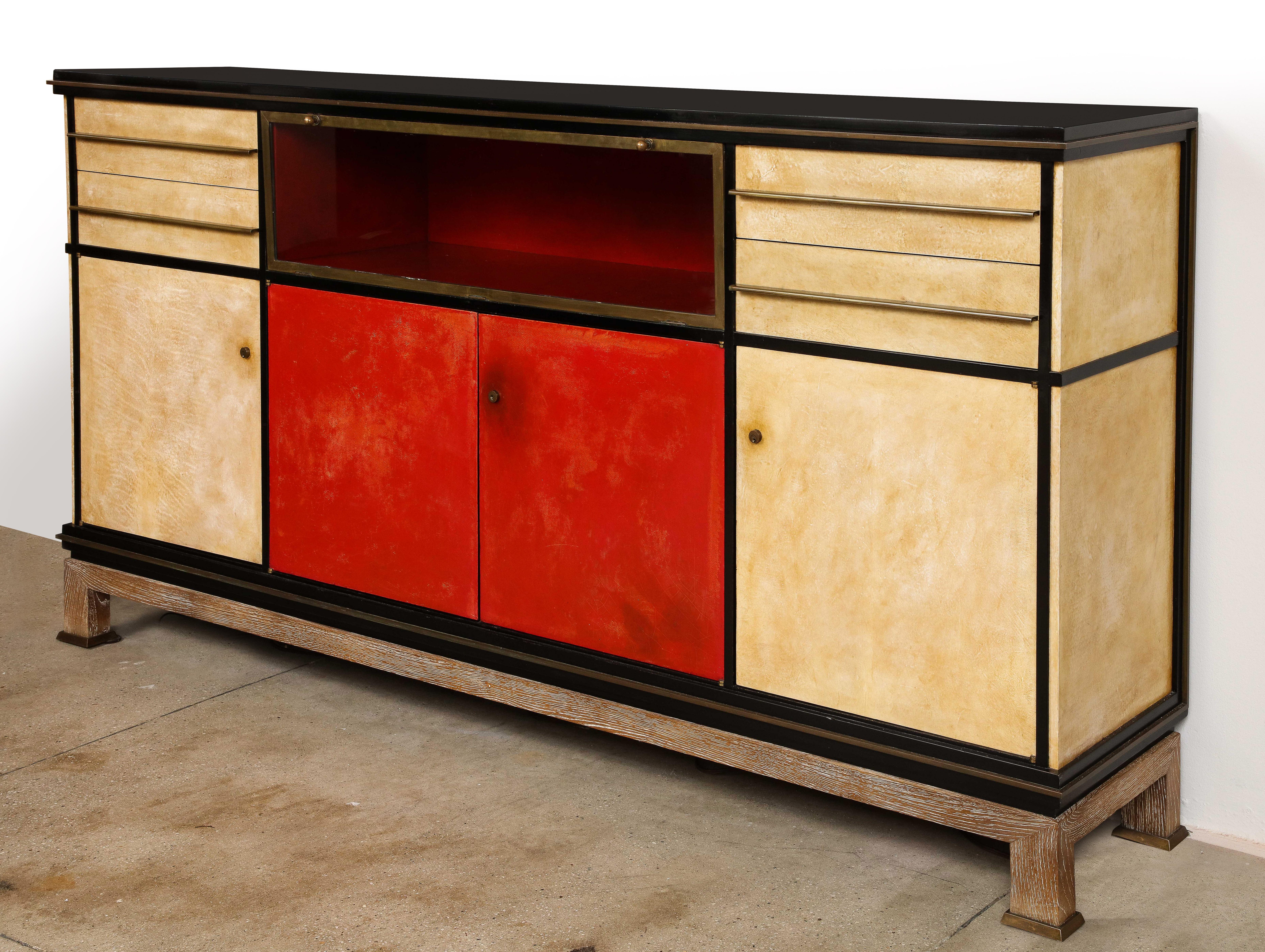 Important black lacquered wood, goatskin and red leather covered credenza by Paul Dupré Lafon, the front and sides decorated with bronze mouldings and drawer pulls. Glass and bronze drop front center vitrine with fitted with a beautiful red