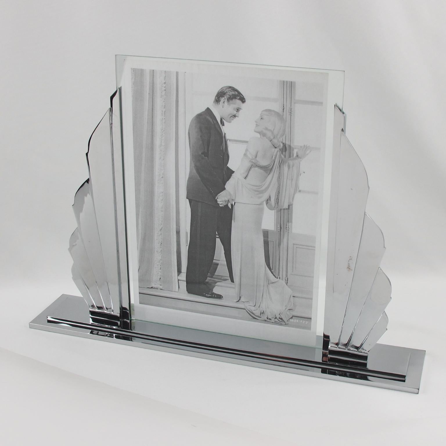 This impressive French Art Deco picture photo frame features a high-end quality build with polished chromed metal boasting a silhouetted stylized sunrise shape with four chrome rays on either side of the picture opening. The base is constructed from