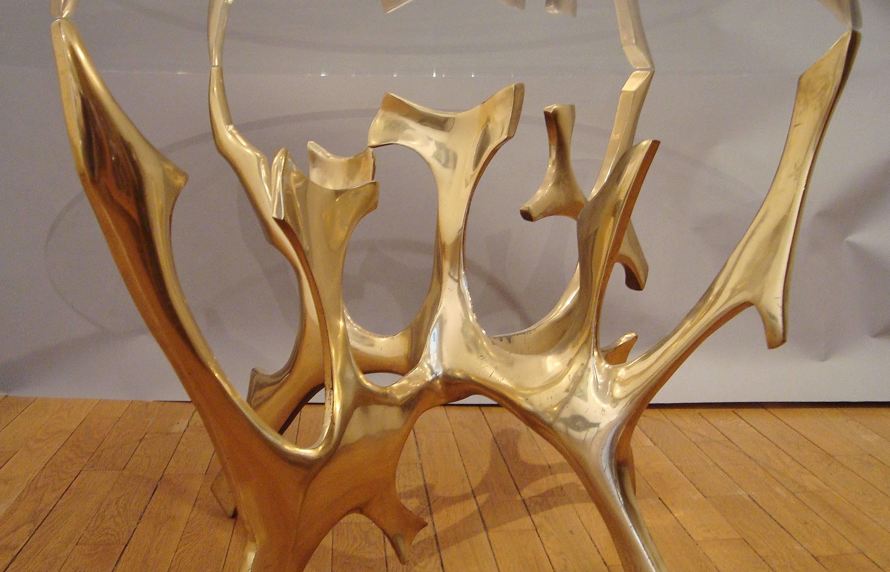 Important gilt polished bronze sculpted table, 1970s, by Fred Brouard (1944-1999)
with a circular clear Saint-Gobain glass top.
Signed.
Bronze height 74 x large 100 cm.
      