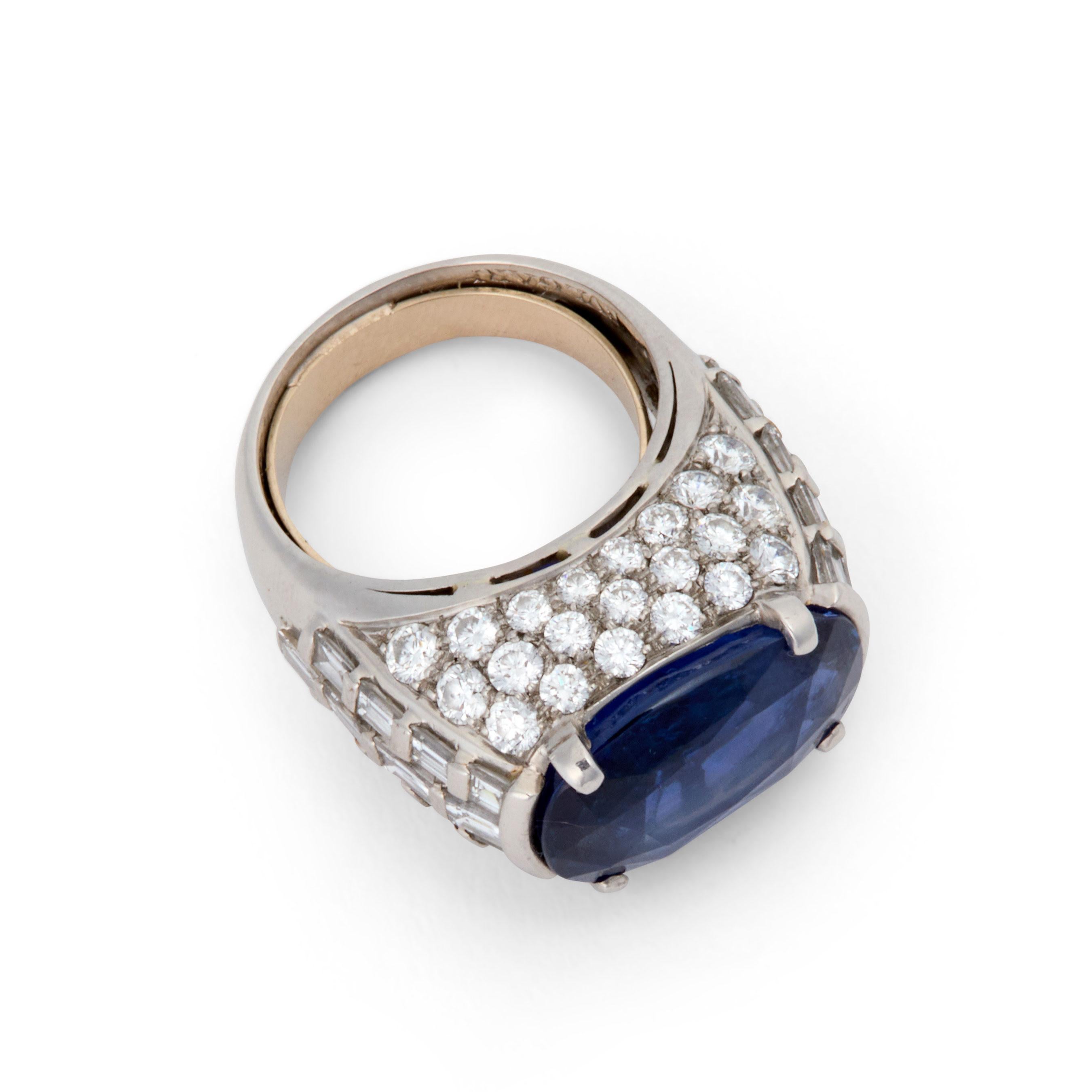 This striking 13.68 carat elongated cushion-cut royal blue sapphire is set in a setting that matches the beauty of the stone.  The stone runs east-west and sits at the top of a stack of round diamonds on the front and back with the sides set with