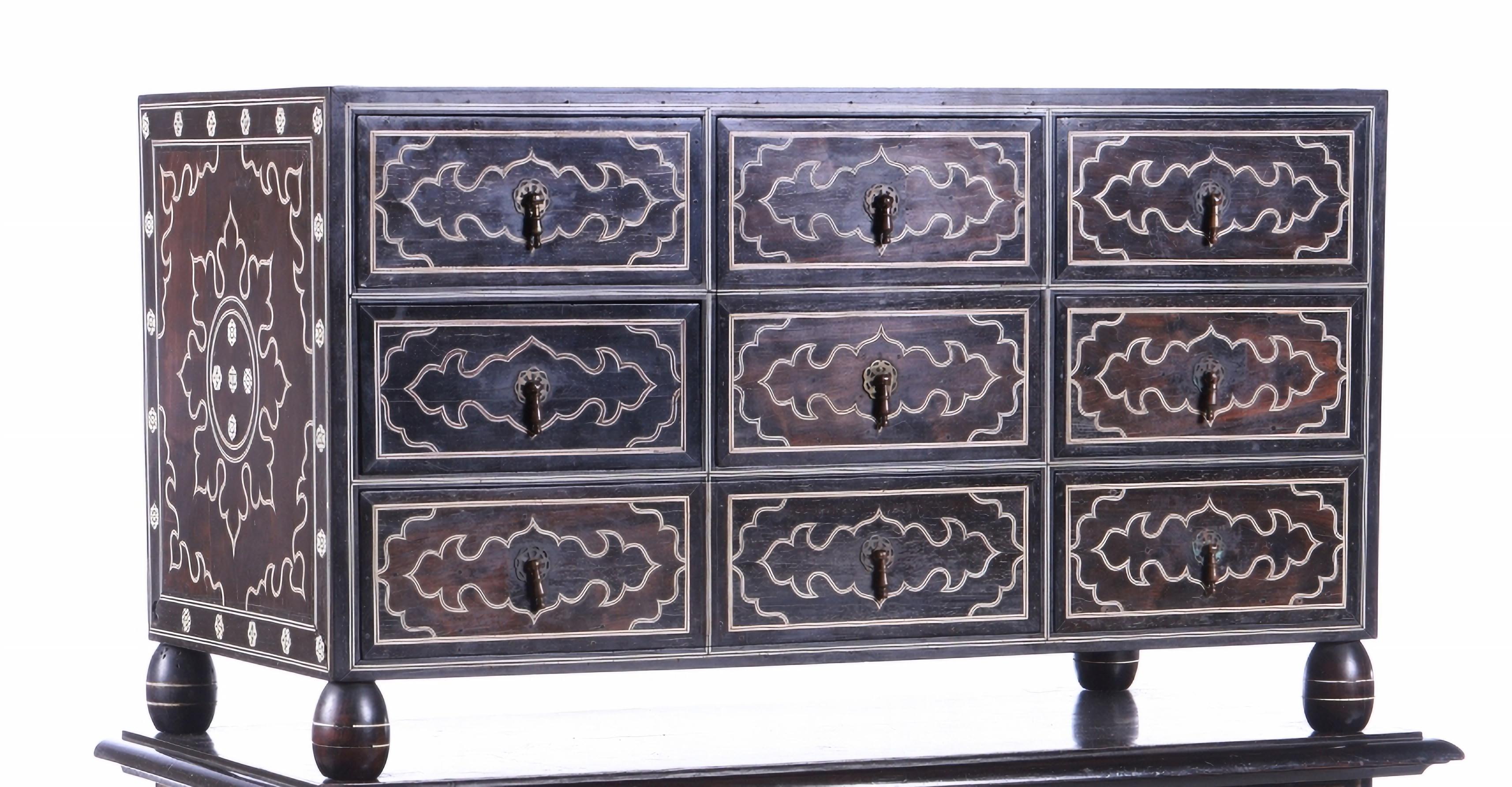 Cabinet counter
Indo-Portuguese - Mogol
17th century,
in teak, ebony and ivory, with eight drawers simulating nine. Decoration representing stylized geometric and floral elements. Brass fittings.
Stands on a back trivet, in wood and