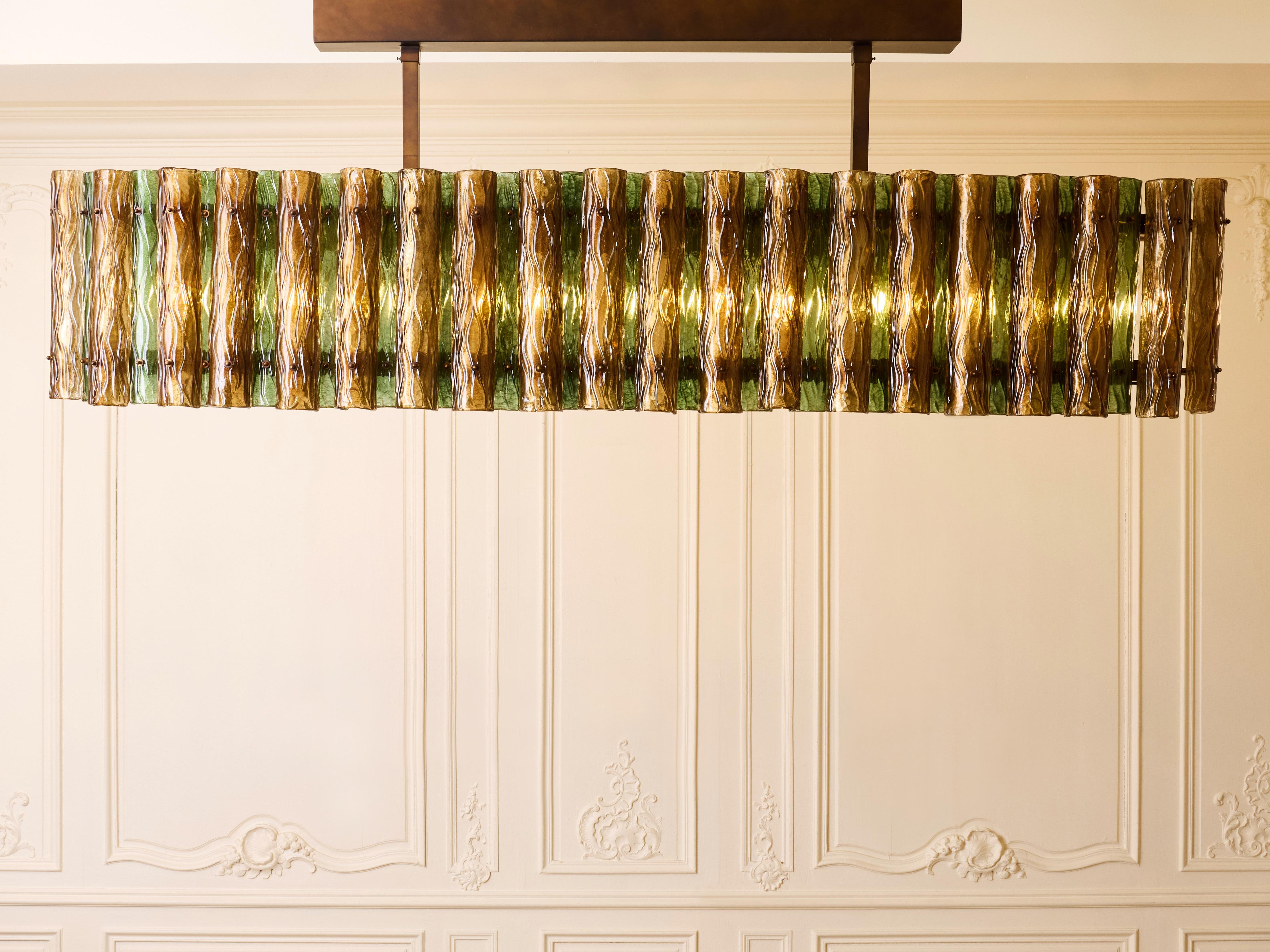 Exceptional long chandelier in patinated brass, with sculpted and tinted Murano glasses by Studio Glustin.
Italy, 2025.