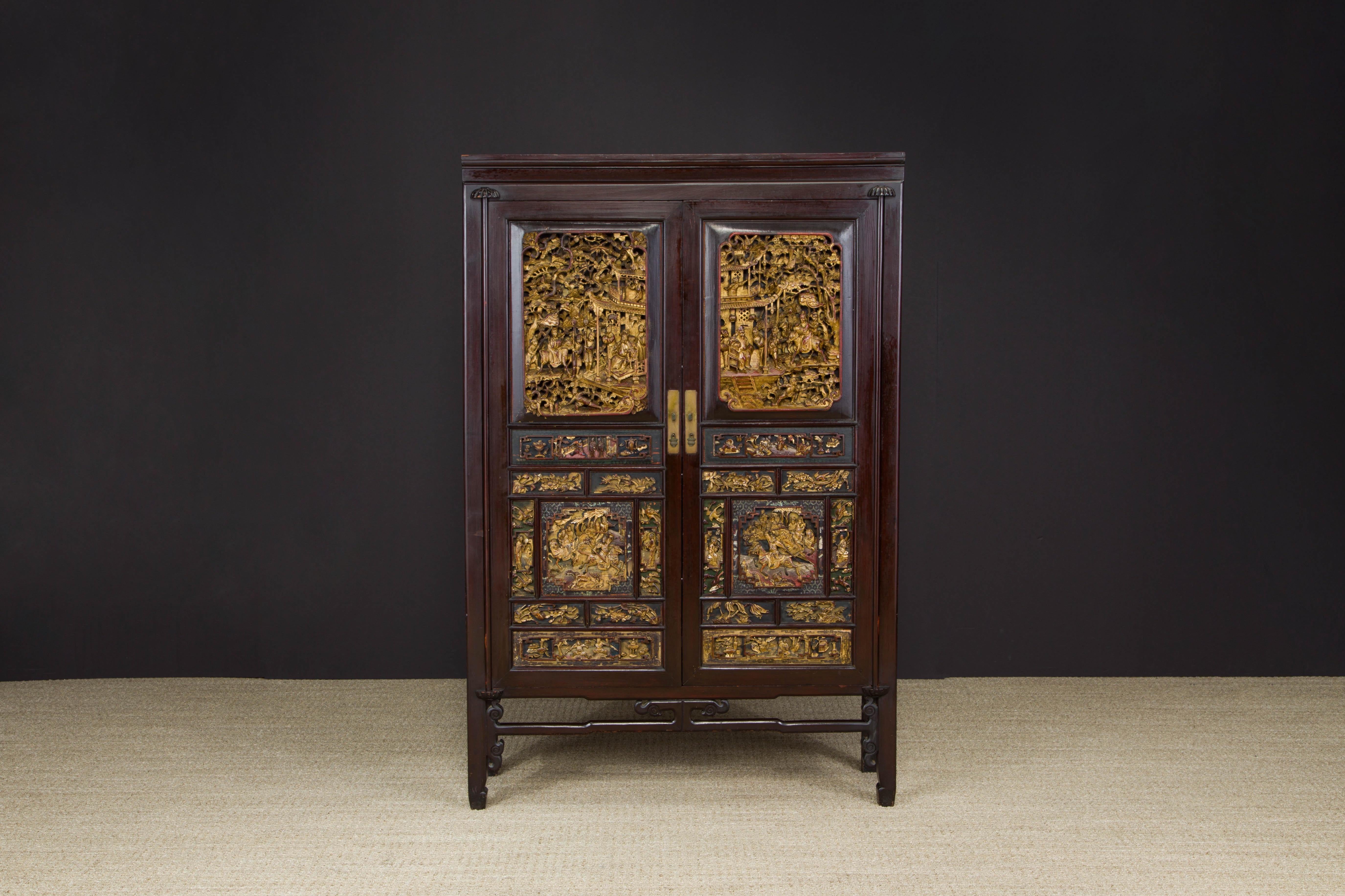 An exquisite custom antique 19th century Qing Dynasty heavily carved Chinese rosewood and elm wooden cabinet with double-doors carved set with gilt and deep relief carved wood panels depicting scenes from historical legends and brass handles