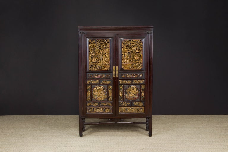 An exquisite custom antique 19th century Qing Dynasty heavily carved Chinese rosewood and elm wooden cabinet with double-doors carved set with gilt and deep relief carved wood panels depicting scenes from historical legends and brass handles