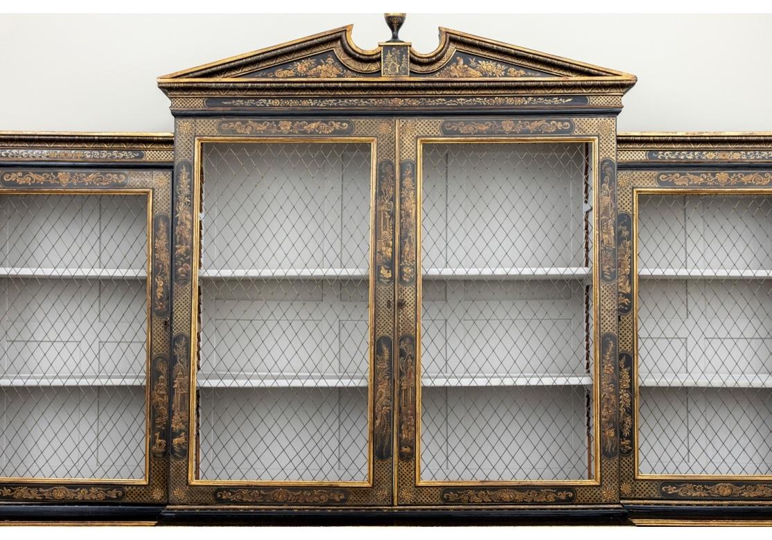 An extraordinary Antique Chinoiserie Display Cabinet dating to the 19th Century. Made in six sections, mounted on a later base. An ebonized cabinet with overall fine chinoiserie gilt decoration. The center section with broken bonnet with fine carved