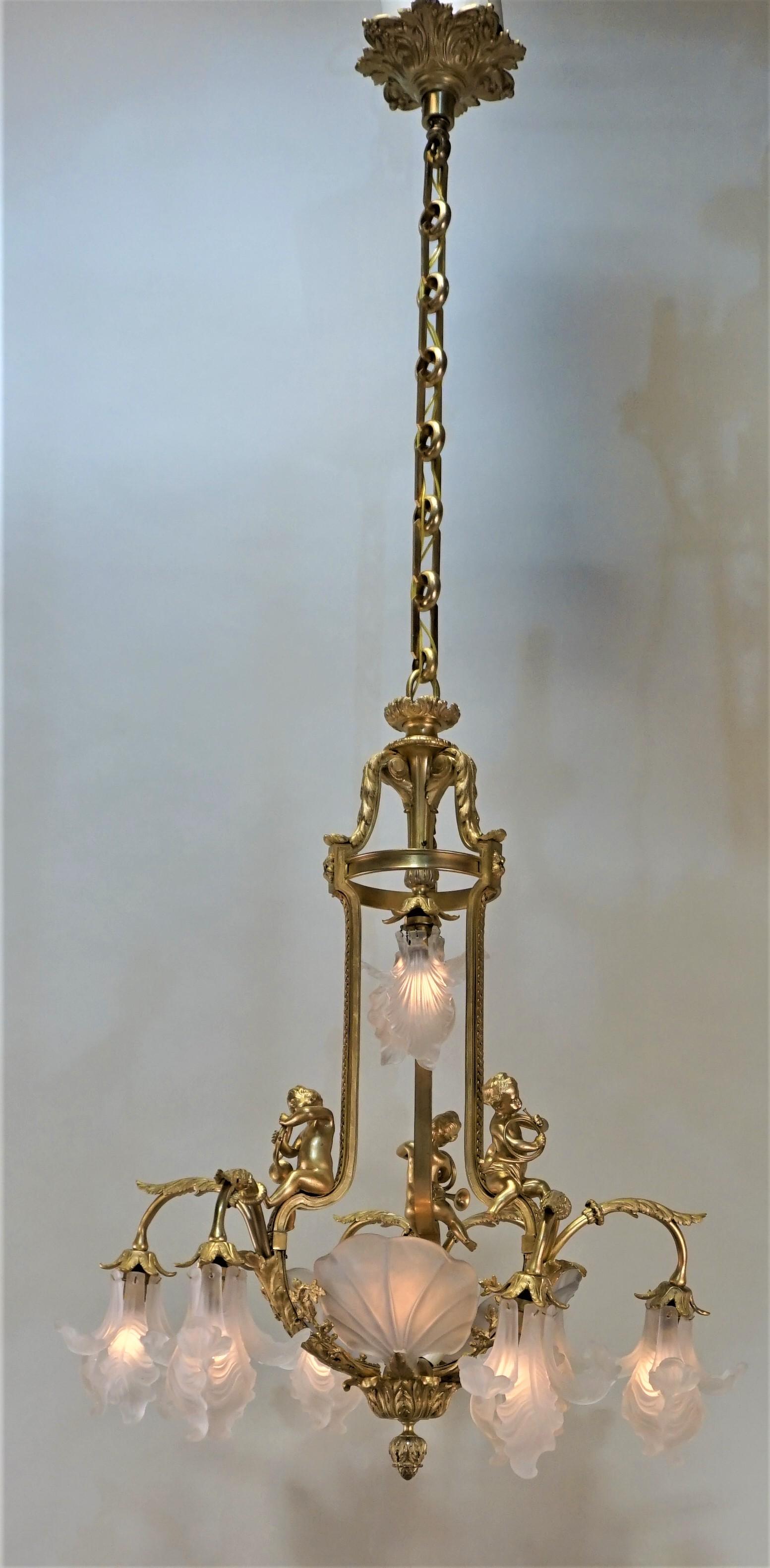 The doré bronze chandelier features three babies playing horn on a double arm light, each light surrounded with six individual clear frost petal in shape of flower, center lights are shield with 3 clear frost leaves.
By E. Mottheau Paris
Total