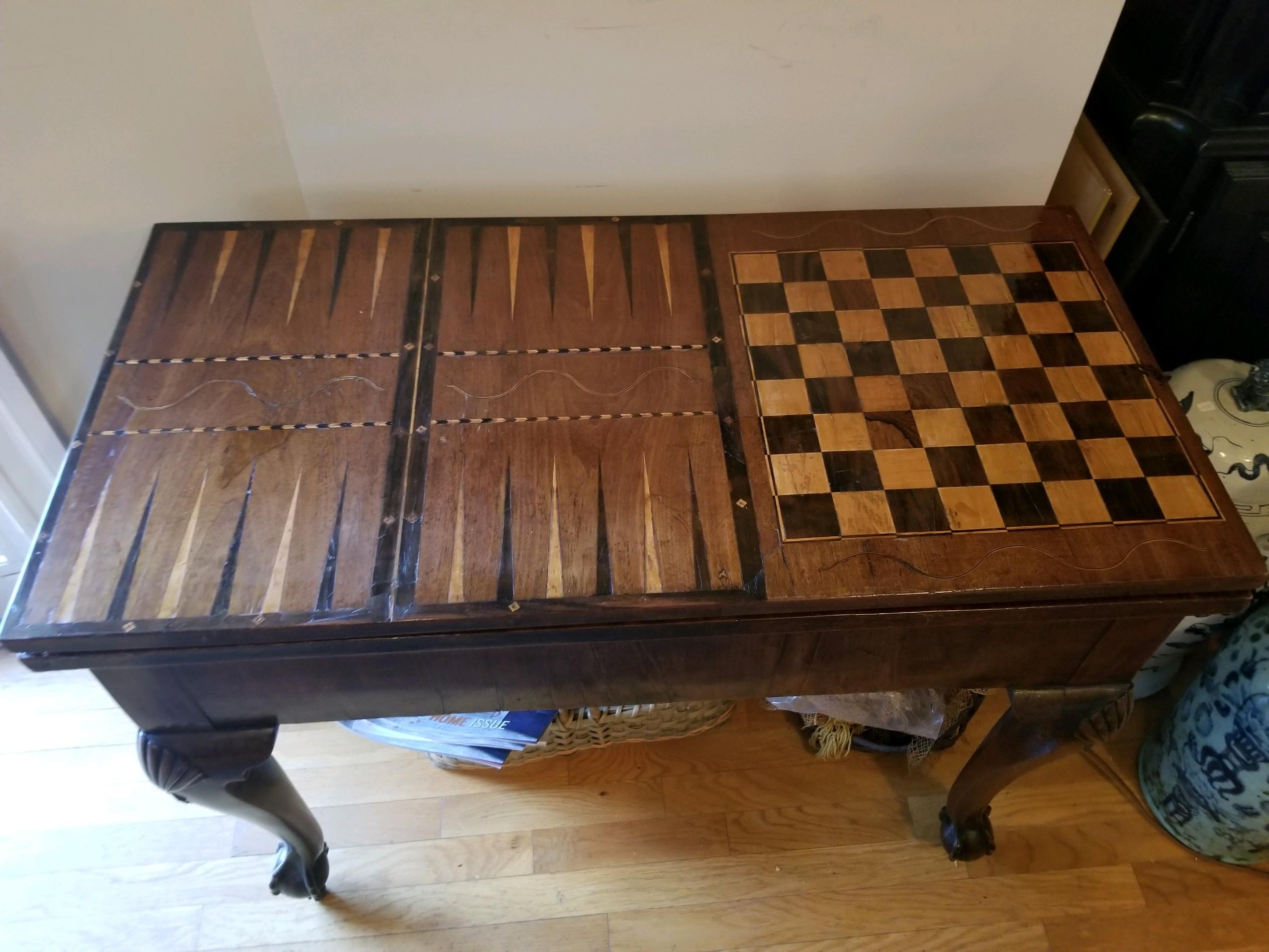 This important George III console gaming table has inlaid woods forming on its top for background and chess/checkers. When pulled from wall and leg is swung open, the flip top creates a card table with cut-in cups for chips/money and by flipping the