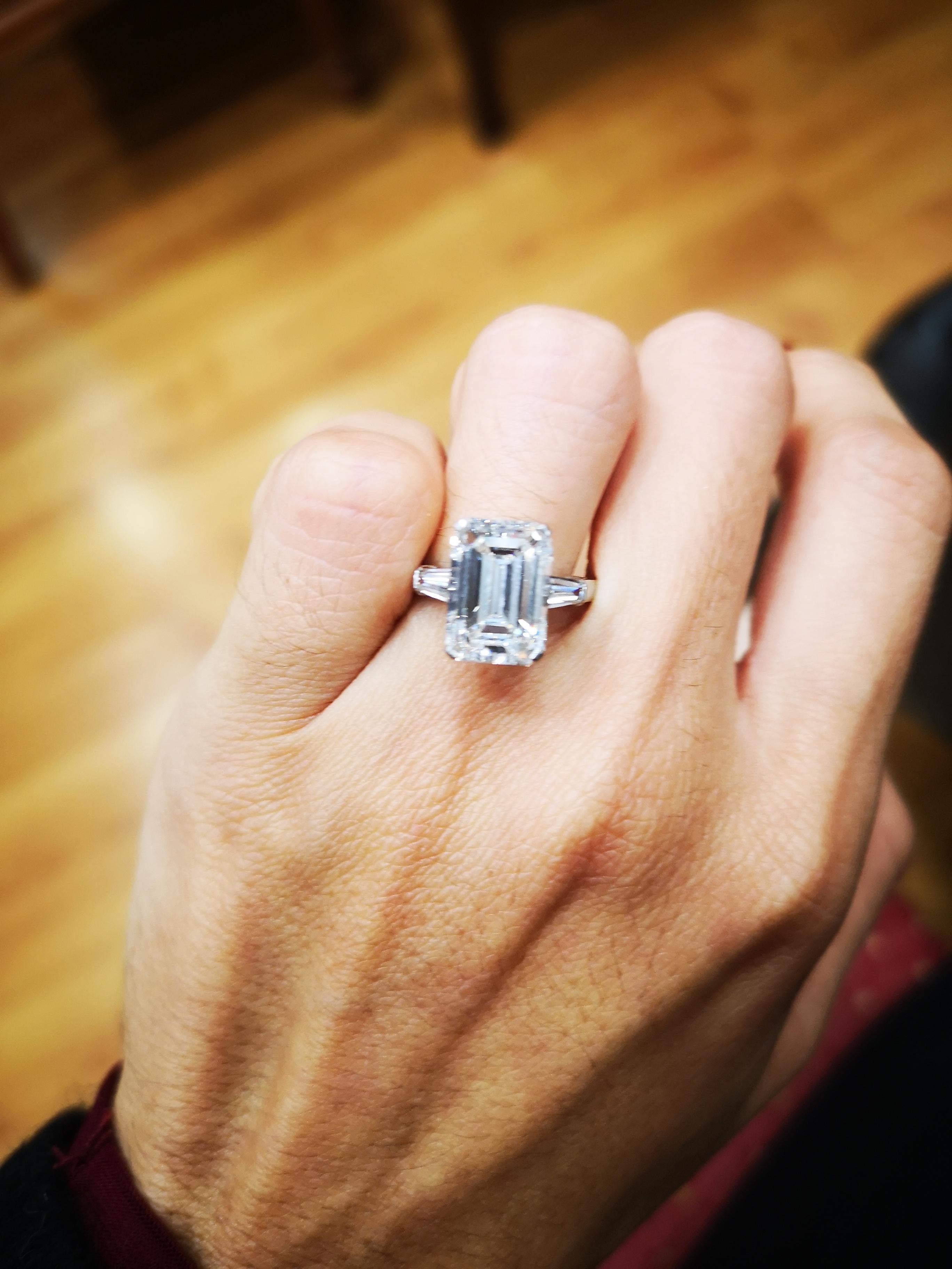 An important and classic engagement ring showcasing a 7 carat emerald cut diamond certified by GIA as J color, VVS2 clarity. Flanking the center diamond are two smaller GIA certified tapered baguette cut diamonds weighing 0.80 carats Accent diamonds