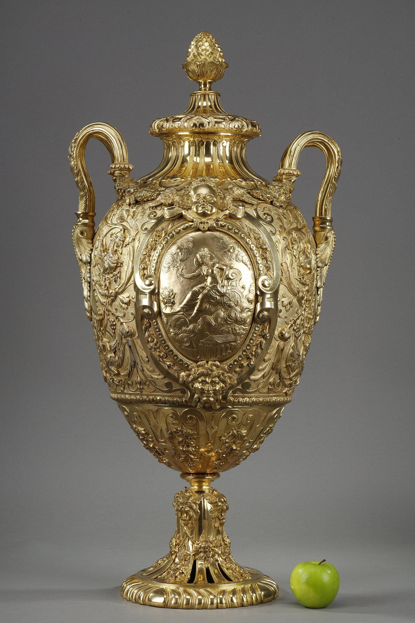 Imponente vaso coperto di forma ovoidale in bronzo dorato, riccamente decorato su ogni lato con un medaglione che racchiude una divinità sul suo carro tra le nuvole, incorniciato da fregi e ghirlande, un putti in alto e una satira in basso.