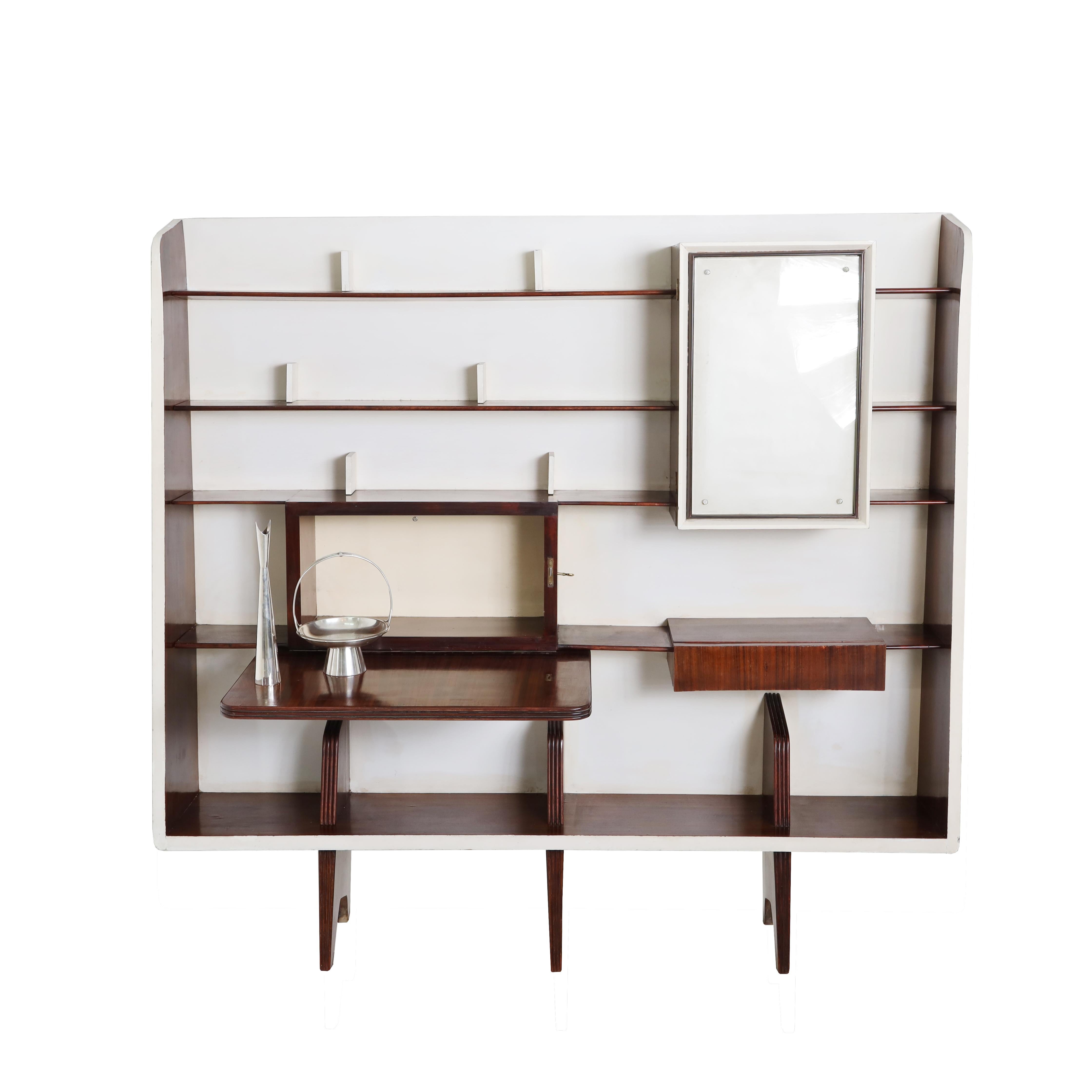 An important rare Gio Ponti Modernist wall unit. Veneered wood, painted wood, mirror glass, brass. Features display shelving, a drop down writing surface and an integrated drinks cabinet with mirrored interior. The wall unit comes with a certificate