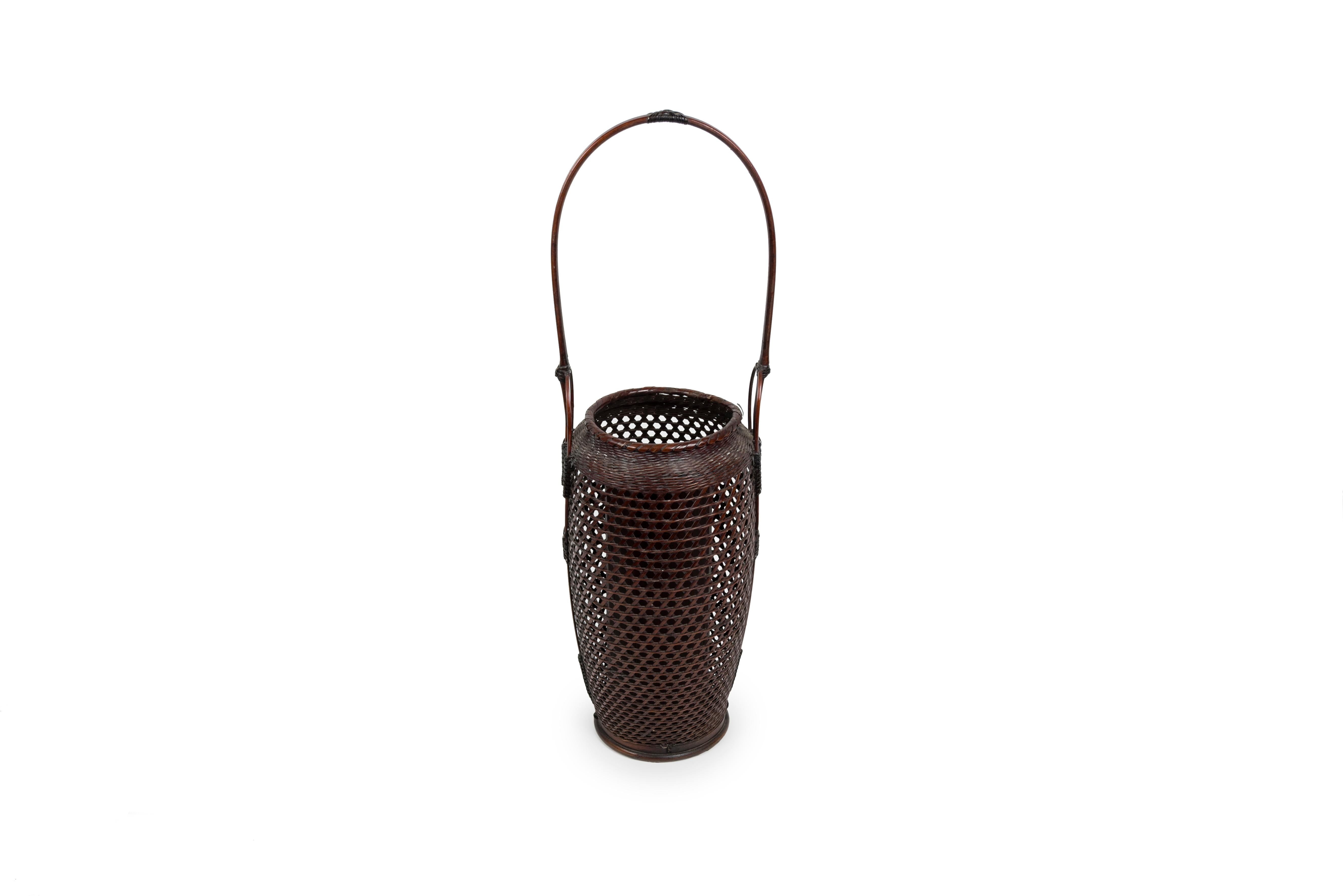 Panier Hanakago pour ikebana en rotin et bambou. Oblongue, arrondie sur les côtés, elle présente un vase en bambou laqué. 
Tressage de rotin dispersé sur le corps, étroitement tissé sur l'épaule. Base et poignée en bambou nouées avec du rotin.