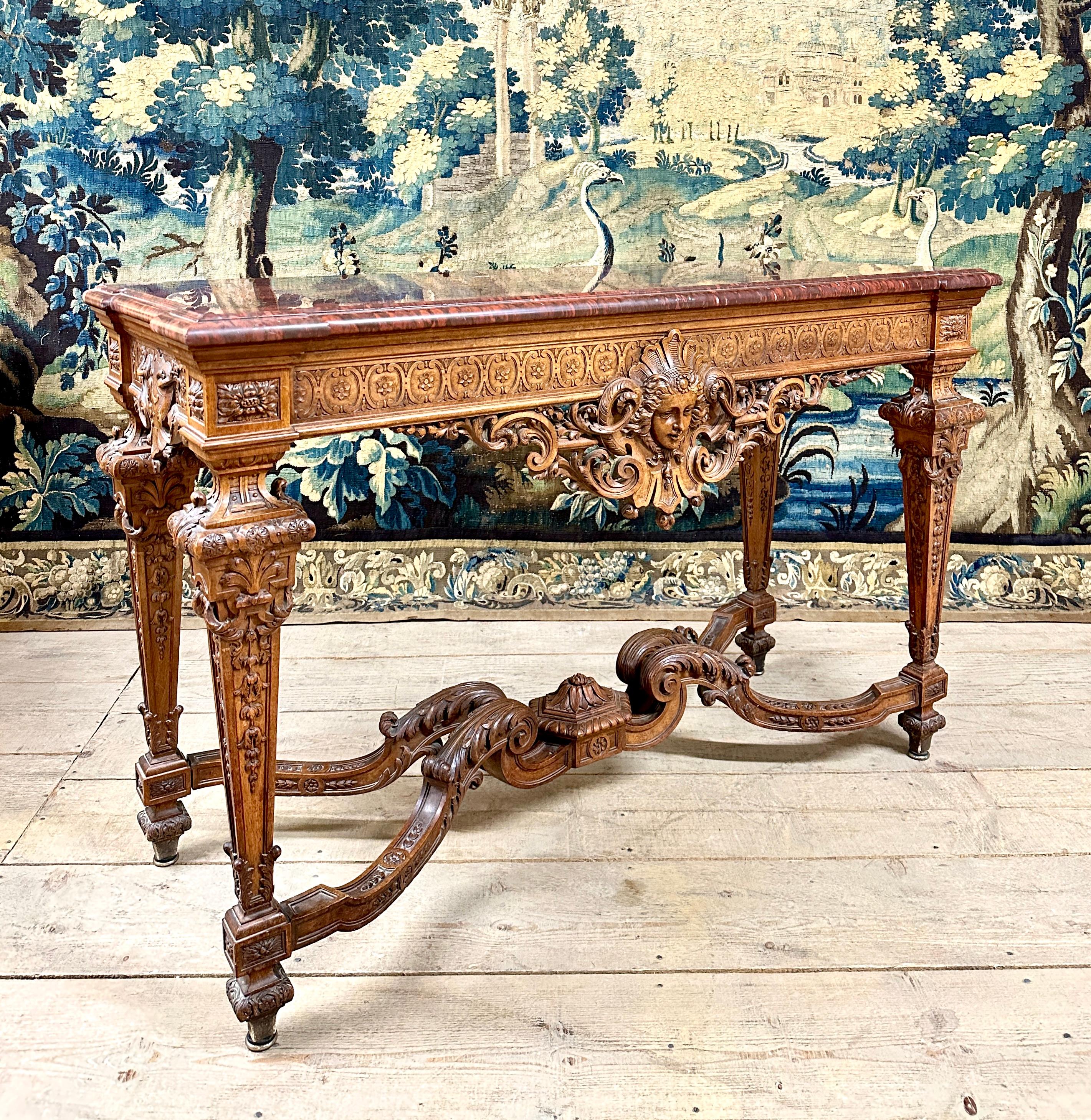 Important walnut console with rich carved decoration in the Louis XIV style, with an important woman's mask on the front crosspiece. The feet are joined by a fully sculpted spacer. This console is topped with a very beautiful cherry red marble slab.