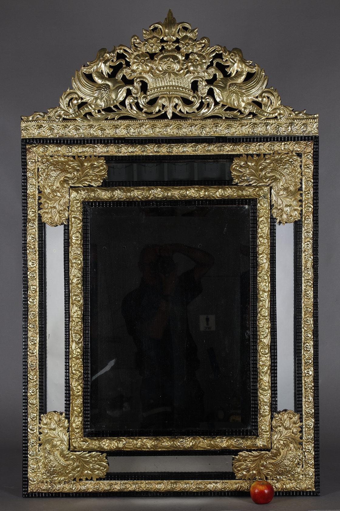 Large Louis XIV style mirror with mirror bars in blackened wood and rich gilded and embossed copper decoration. The pediment is adorned with a motif of a basket of overflowing flowers surrounded by two winged chimeras with open mouths. The central