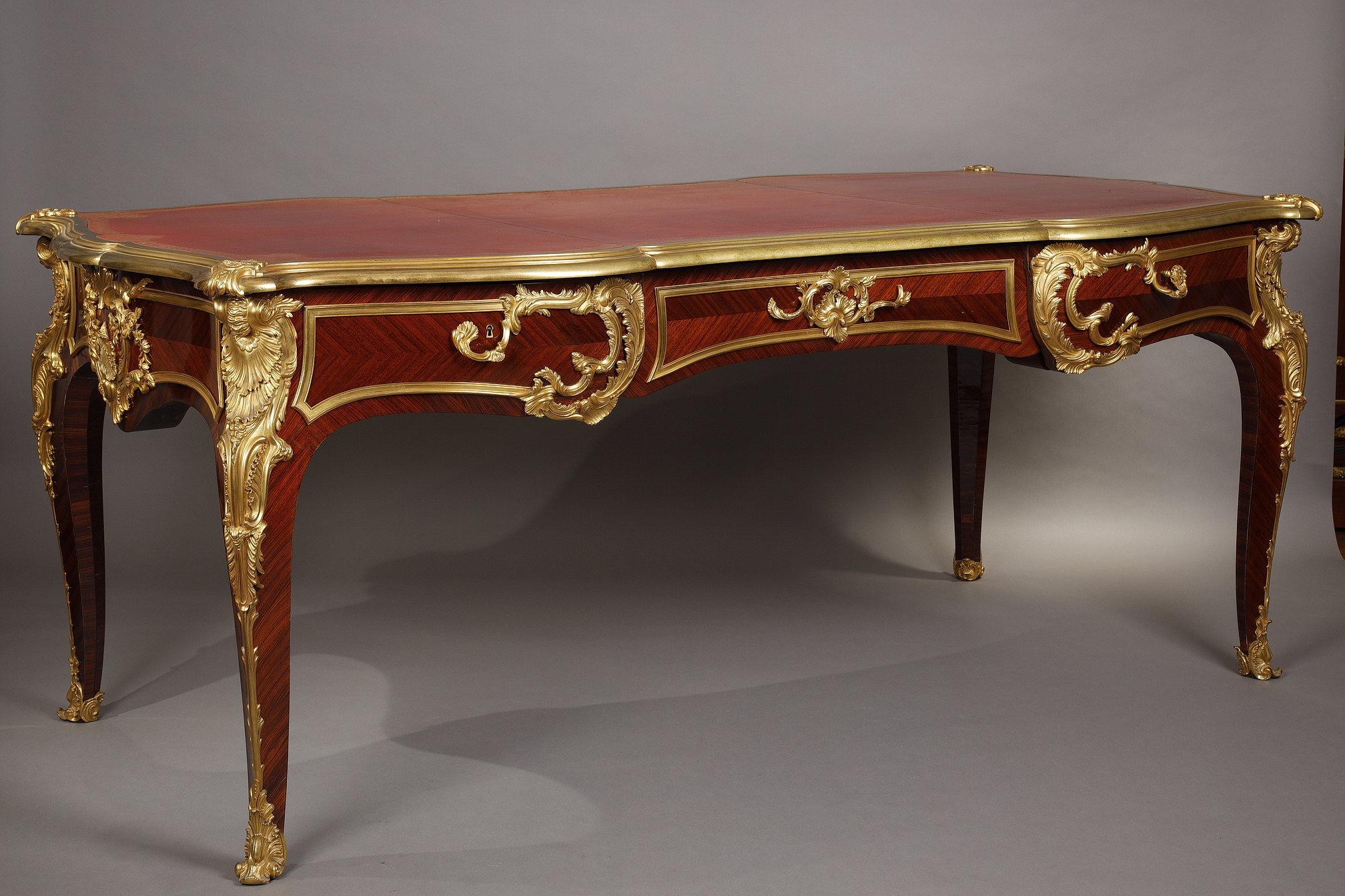 Large veneered wood flat desk attributed to G. Durand, opening with three frieze drawers. Mounted with Rocaille style chiseled ormolu representing shells, foliage and flower garlands. Raised on four cabriole legs ornamented with chiseled