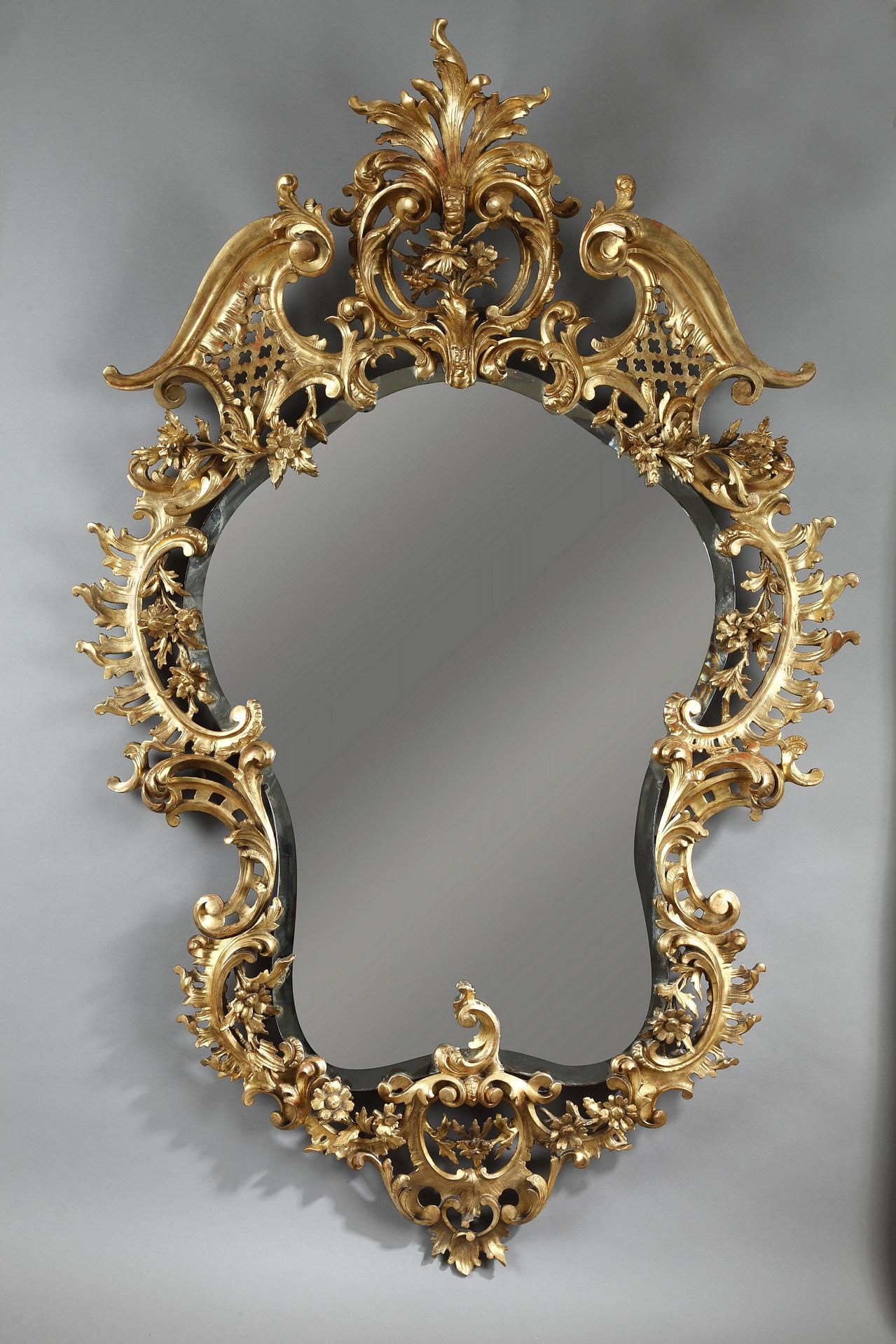 Elegant sculpted giltwood mirror, of curved shape, with a rich rocaille openwork decoration of flowers, scrolls and acanthus leaves.