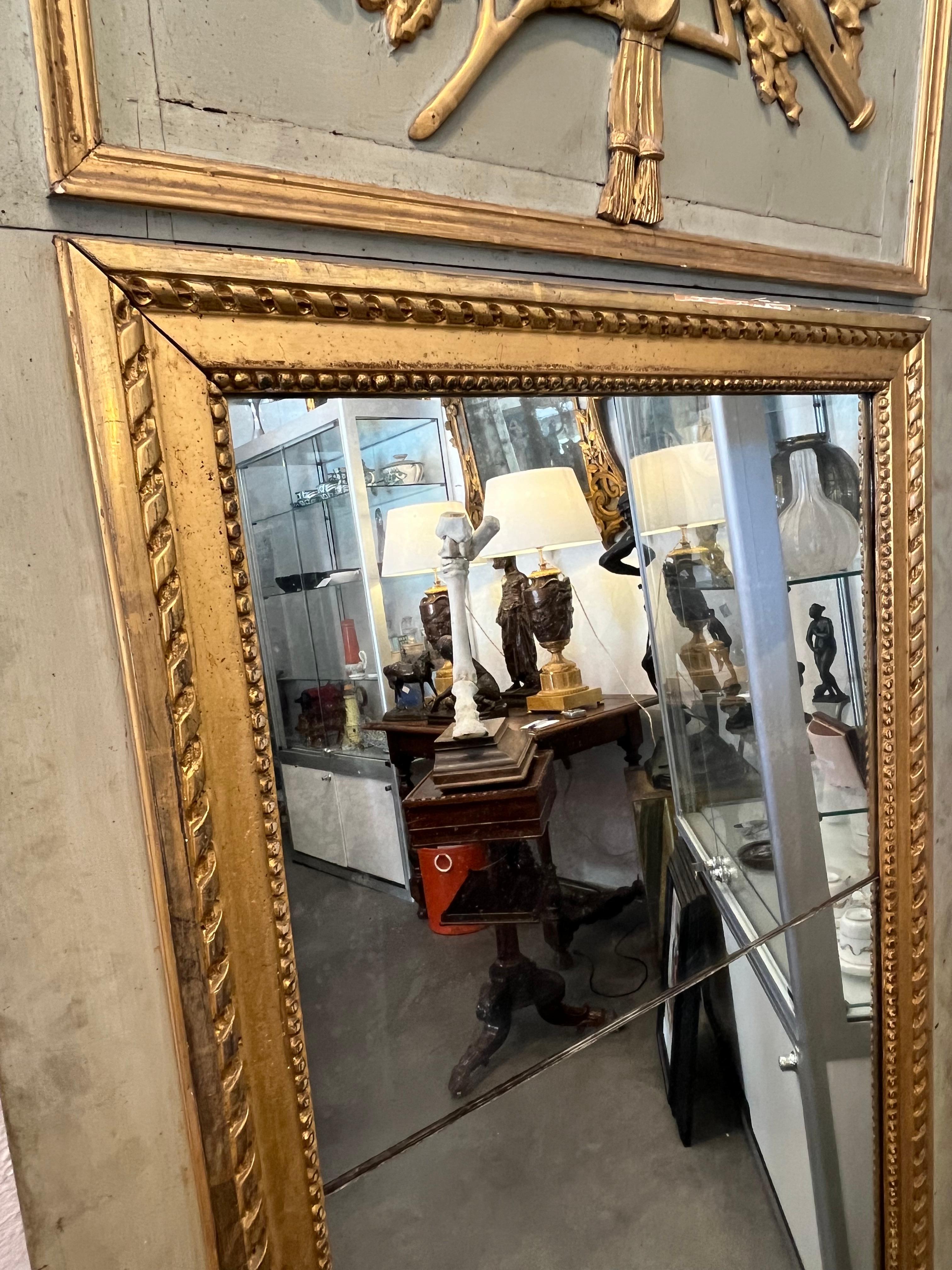 Very beautiful old overmantel mirror from the Louis XVI period (see our article on the Louis XVI style) made during the 18th century in carved, painted and gilded wood. The upper part is carved with musical instruments and laurel branches. The