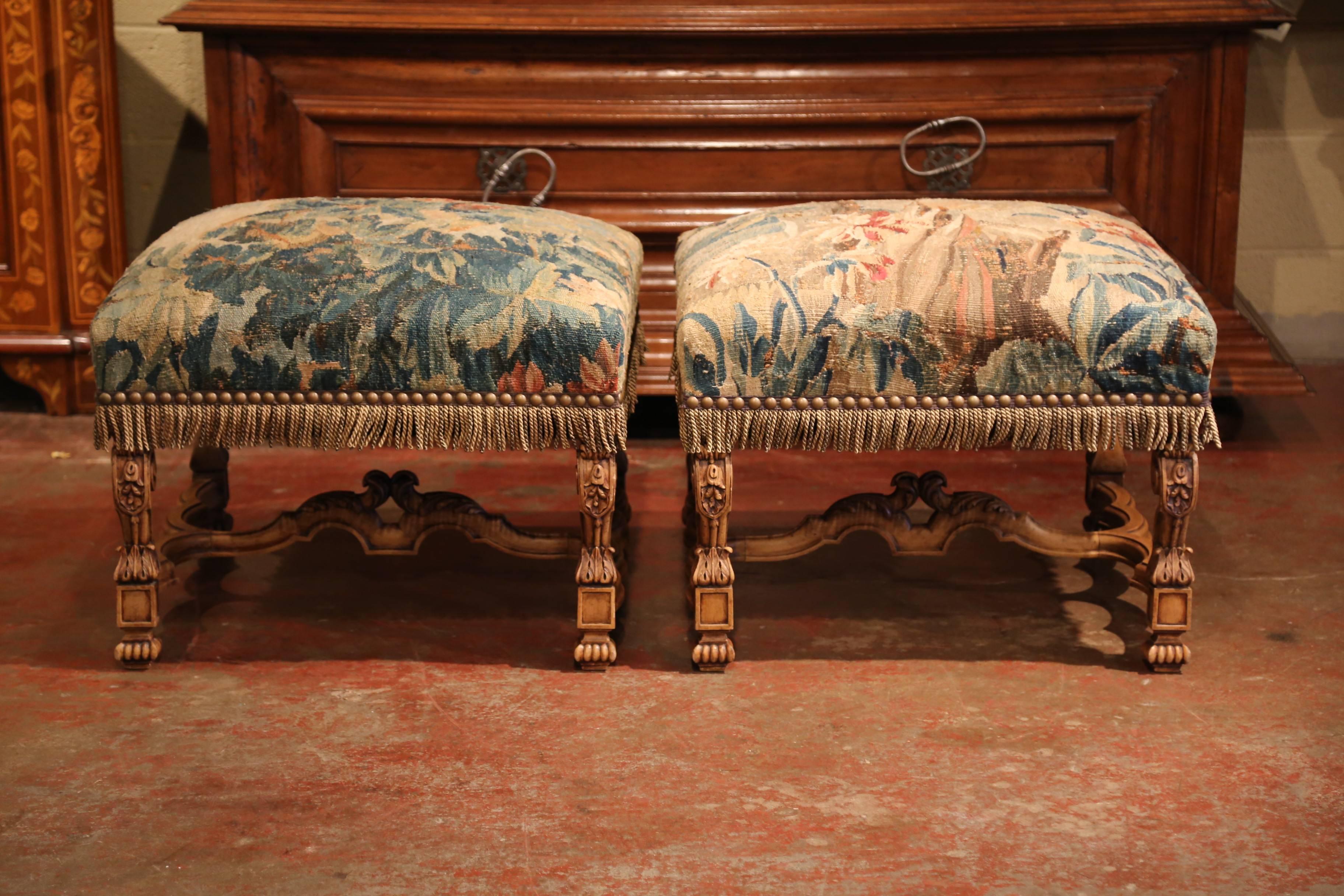 Crafted in southern France circa 1870 and almost square in shape, the elegant fruit wood ottomans stand on four carved legs embellished with an intricate stretcher and central finial. Both pieces are upholstered with 18th century Aubusson verdure