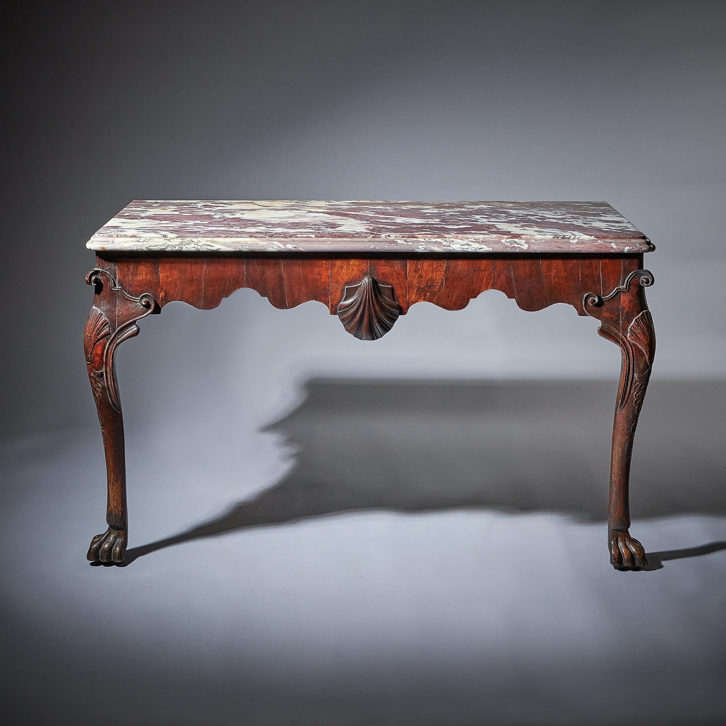 A rare and important pair of George II irish walnut console tables
C.1730. Ireland

Each with a moulded breccia viola top, above a shaped frieze, centred with a carved scallop shell, on scroll, shell, leaf and husk capped legs and lion's paw
