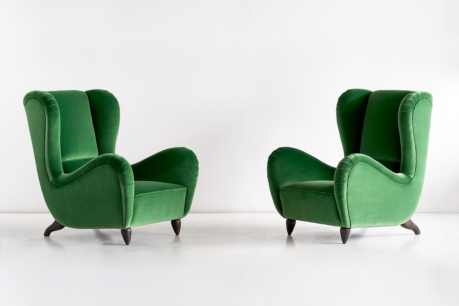 This sumptuous pair of armchairs was designed for a private residence in Milan and produced in the mid-1940s. The organically curved lines and sculptural wooden legs create a striking presence. The generous proportions, the high winged back and the