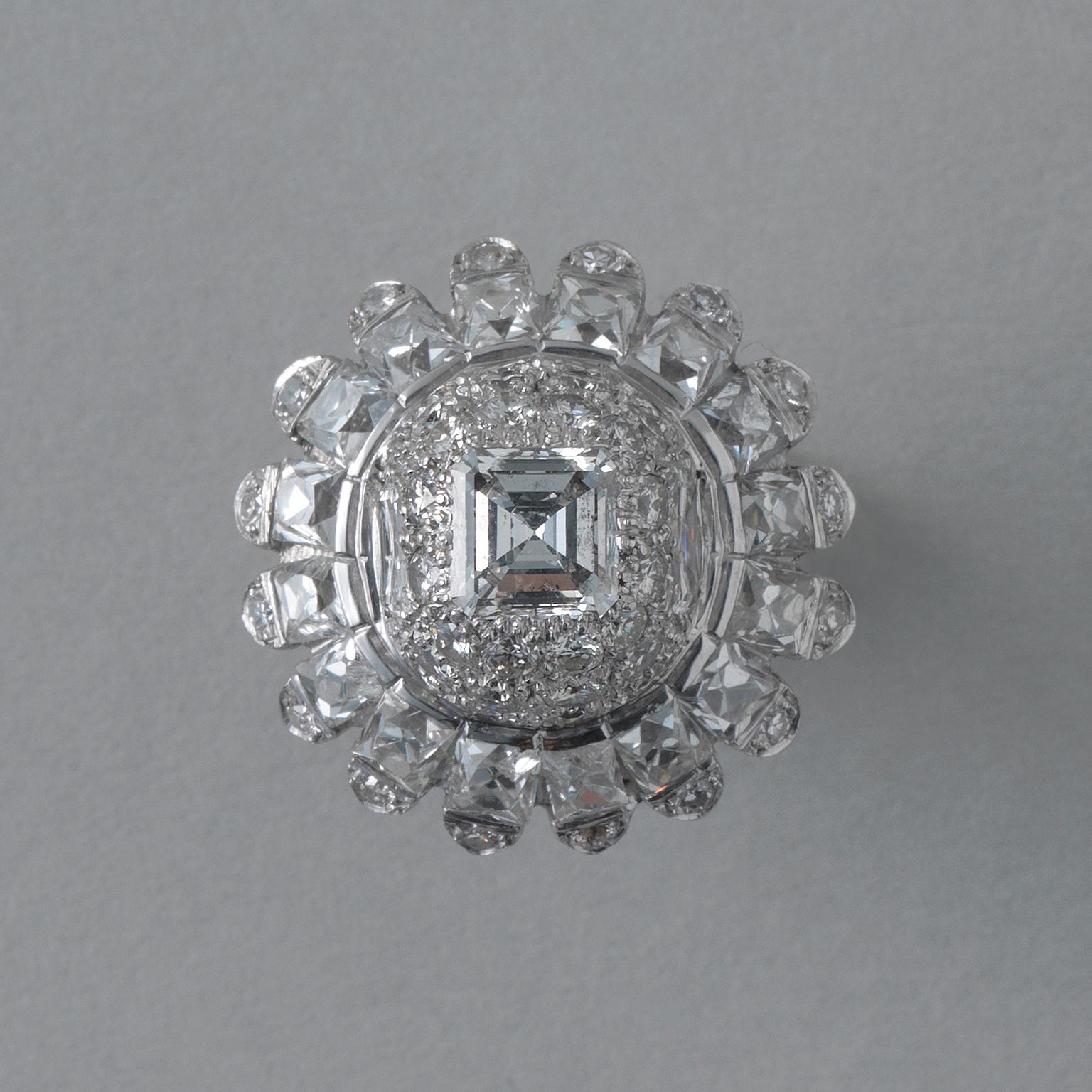 A platinum cocktail ring in the shape of a flower with a high dome with 40 brilliant-cut and 3 large carré-cut pavé-set diamonds (two app. 0.9 carats H-I, VS and I, SI; one centre stone app. 1.35 carats G-H, VS). The petals are set with 16