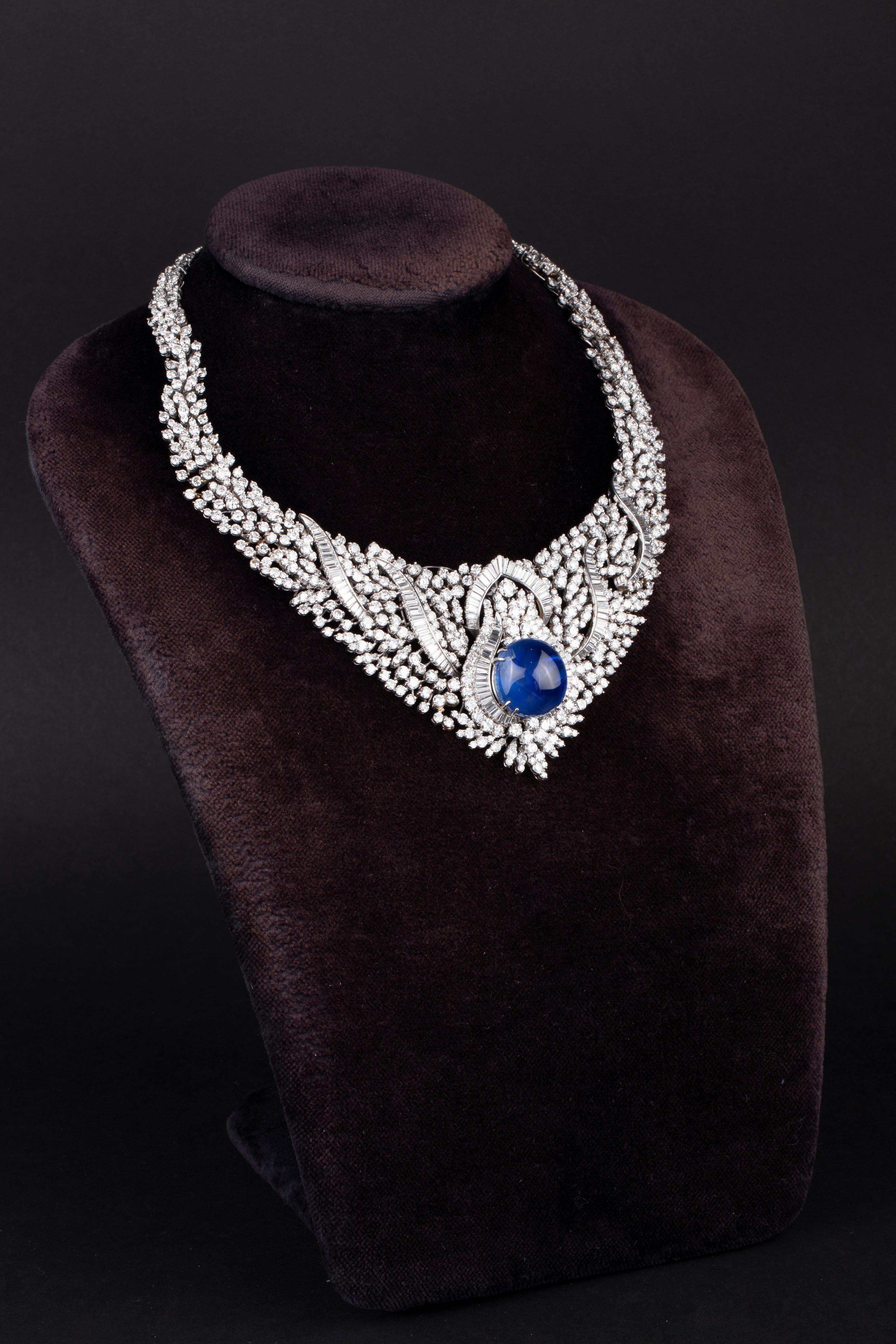 A stunning bib necklace in white gold centering a 39.4 carat blue cabochon sapphire framed by 50 carats of round brilliant and emerald cut diamonds. Um 1950er Jahre.