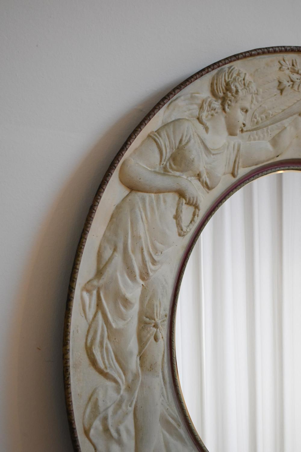 Specchio rotondo con cornice in lamiera sbalzata decorata con allegorie femminili e un cartiglio con la scritta LLC in un cartiglio. Francia, anni '10.