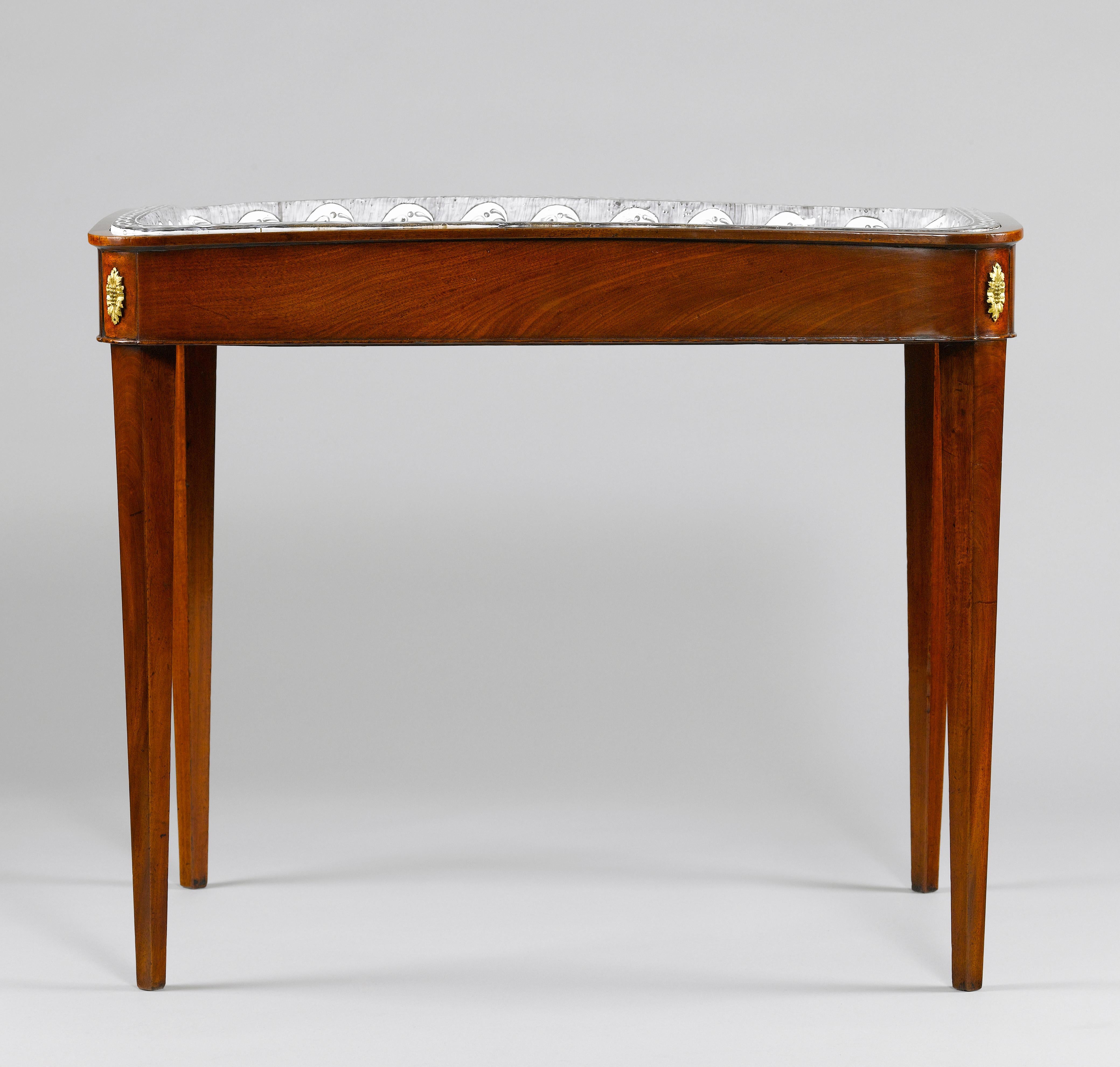 A rare faience topped Rörstrand tea table. The dished, moulded and shaped rectangular top decorated with a harbour szene painted in shades of grey (grisaille painting), on an elegant mahogany stand, with a candleslide on each side, on square