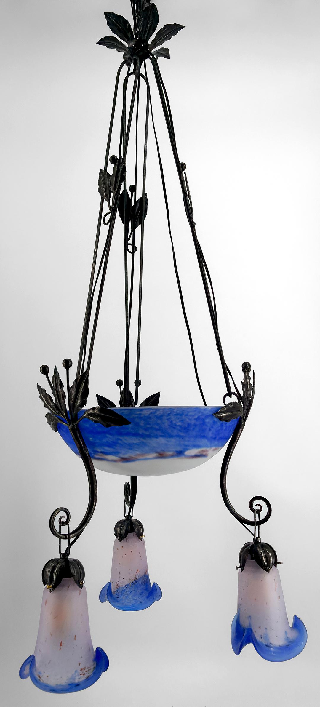We present to you an exceptional chandelier, a centerpiece of the Art Deco style, perfectly combining forged iron and blue blown pâte de verre. 

This chandelier, with its elegant and refined lines, will bring a touch of sophistication and