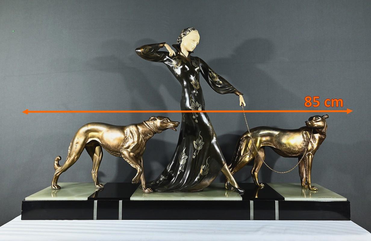 Escultura criselefantina muy grande y elegante de una mujer paseando con sus galgos, firmada por Menneville y Rochard (Ugo Cipriani e Irenée Rochard). La joven fue modelada por Cipriani y los galgos por Irénée Rochard. Este grupo descansa sobre una