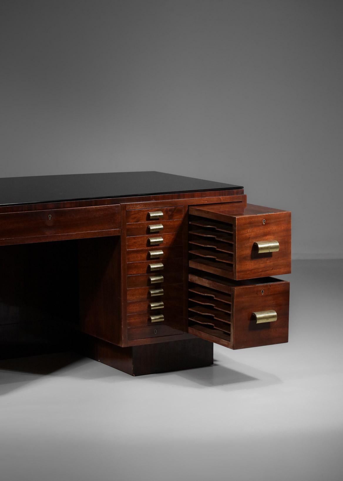 Imposing 1950's French modernist desk. Structure in solid mahogany and veneer, top in black glass. It is composed of a central drawer, two columns of ten drawers each, two additional file drawers on each side and a retractable shelf on the left