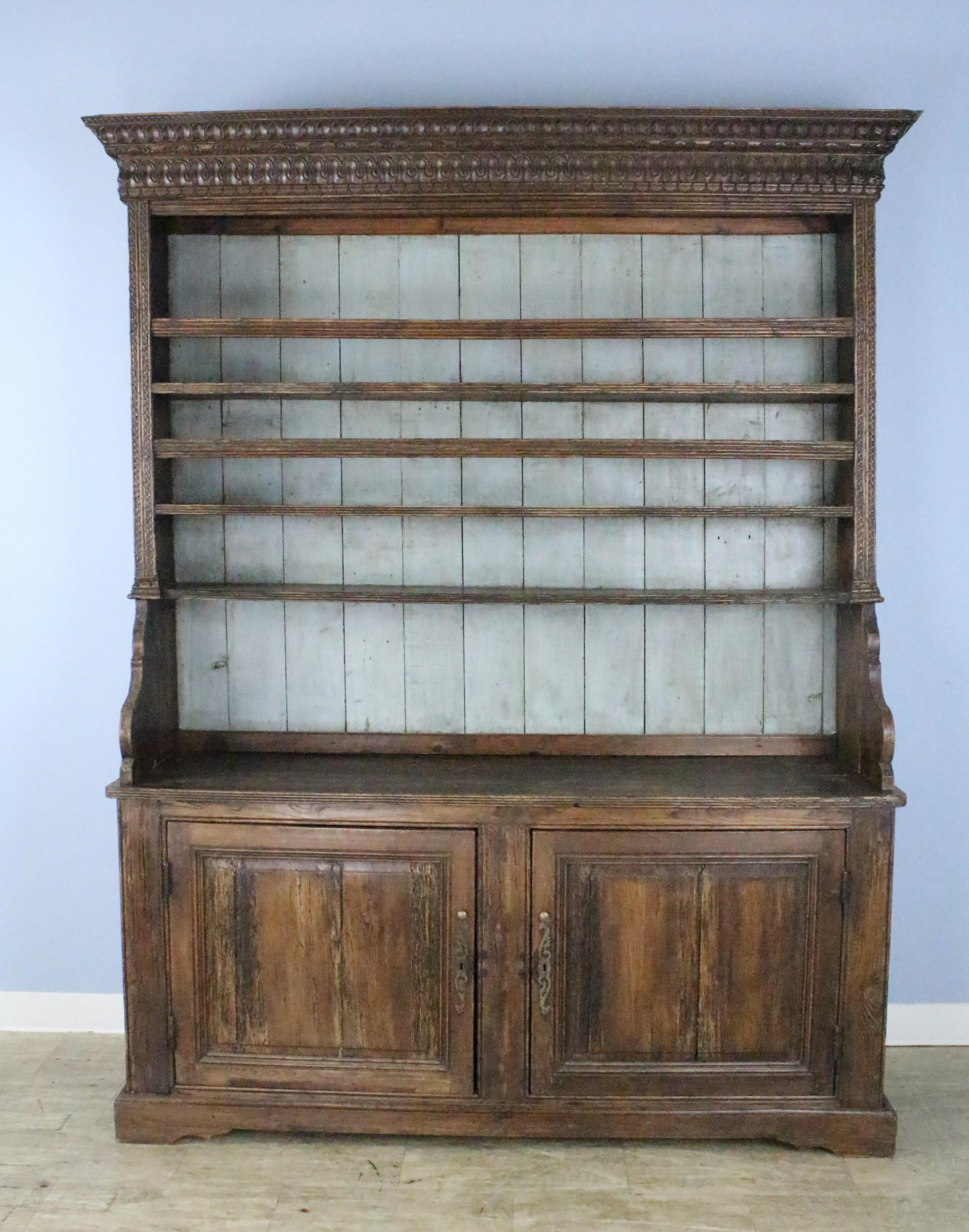 A well distressed French pine dresser, grand in scale. Both the base and the shelf, complete with three plate racks, each 9 inches deep, are solid and sturdy. The cupboard is deep and roomy, and the doors shut nicely. The back of the plate rack has