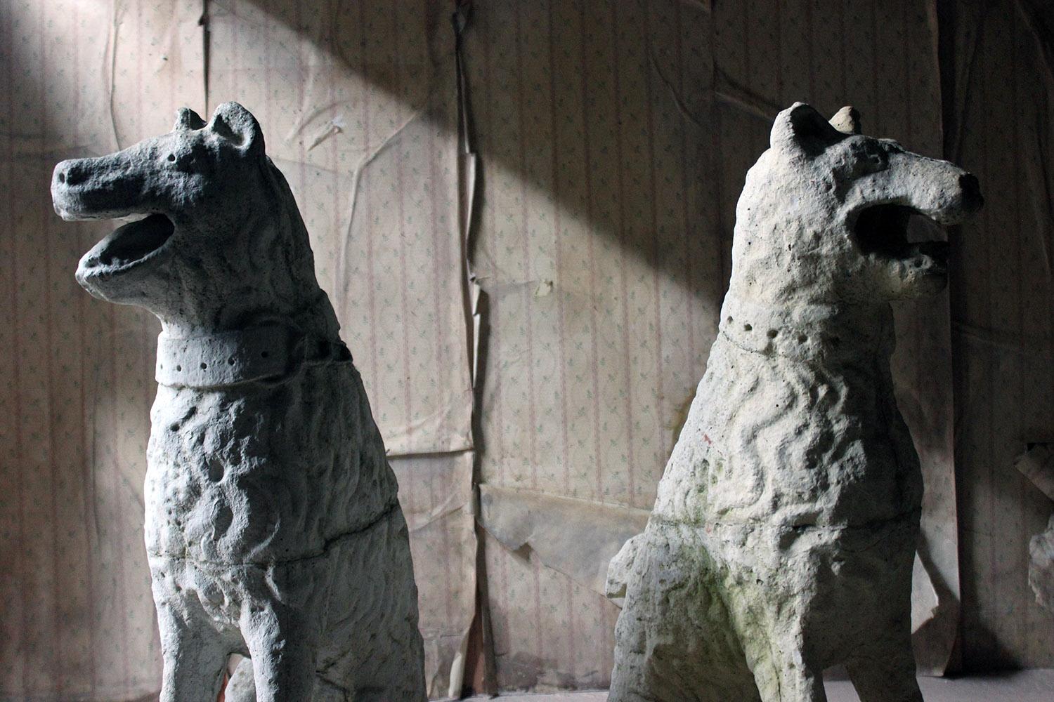 The large and imposing pair of cast stone opposing dogs or hounds, of unusual form and copied from a medieval design, each with open mouths and lolling tongues, their expressions somewhat crazed, with large collars and looped chains, seated alert,
