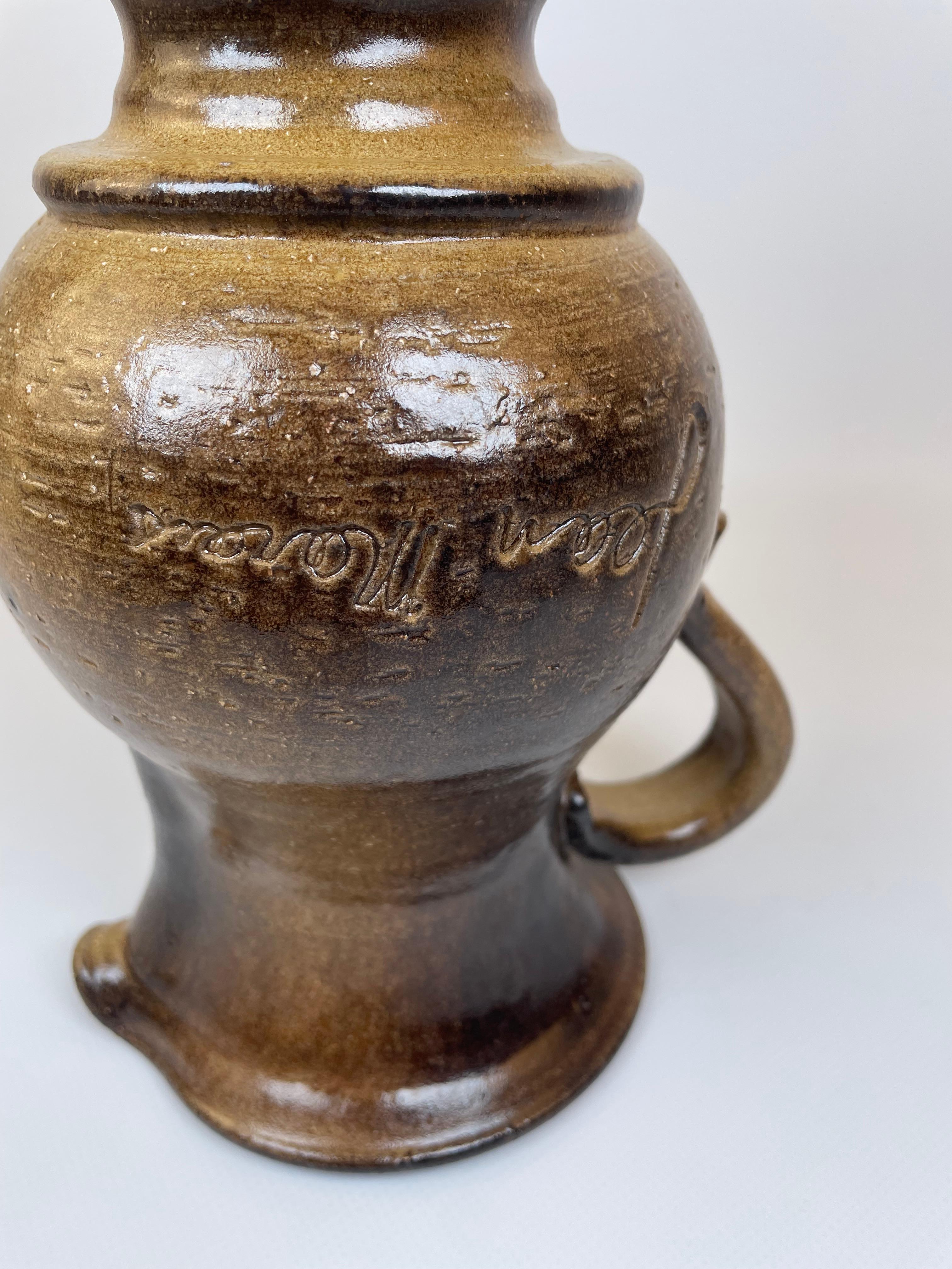 This ceramic pitcher, crafted by Jean Marais in Vallauris (France), reflects a rustic yet refined aesthetic. Its rich brown glaze enhances the curves and smooth surface, while the artist's signature etched into the body signifies its authenticity.