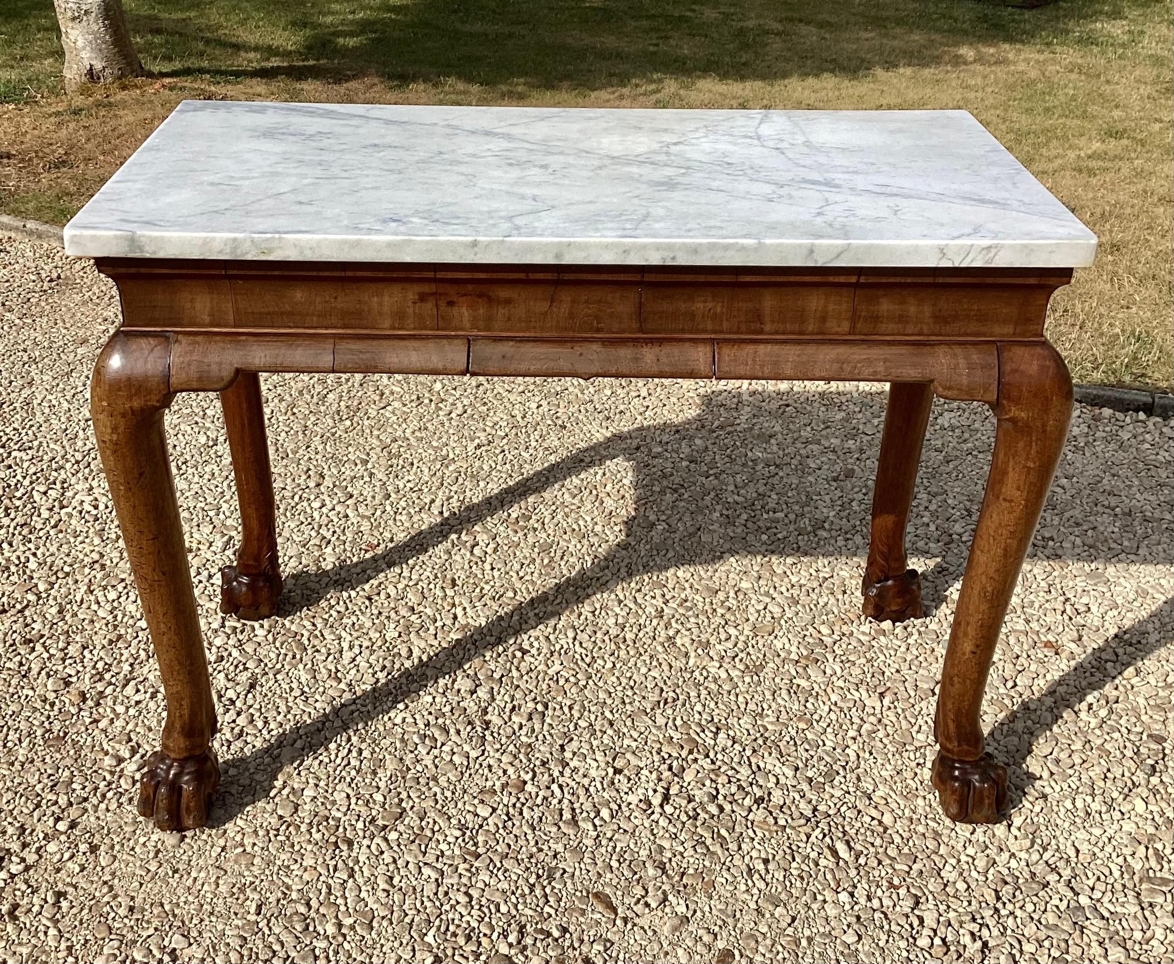 A bold Irish George II marble-topped red walnut side table, the rectangular Carrara marble top above a cavetto frieze with half-round cross grain mouldings, raised on powerful cabriole legs with flared ankles terminating on exceptional oversized