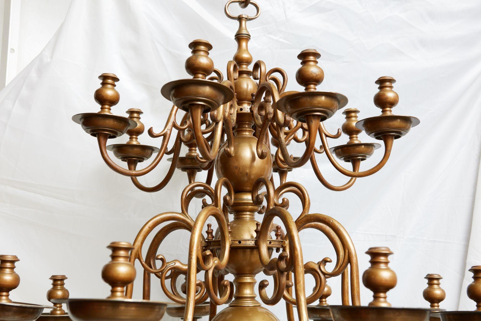 Beau, rare et impressionnant lustre en laiton du XVIIIe siècle, composé de trois niveaux de huit bras en volute, pour un total de 24 bras, tous avec des douilles de bougie et des gouttières d'origine, les bras étant maintenus en place par des
