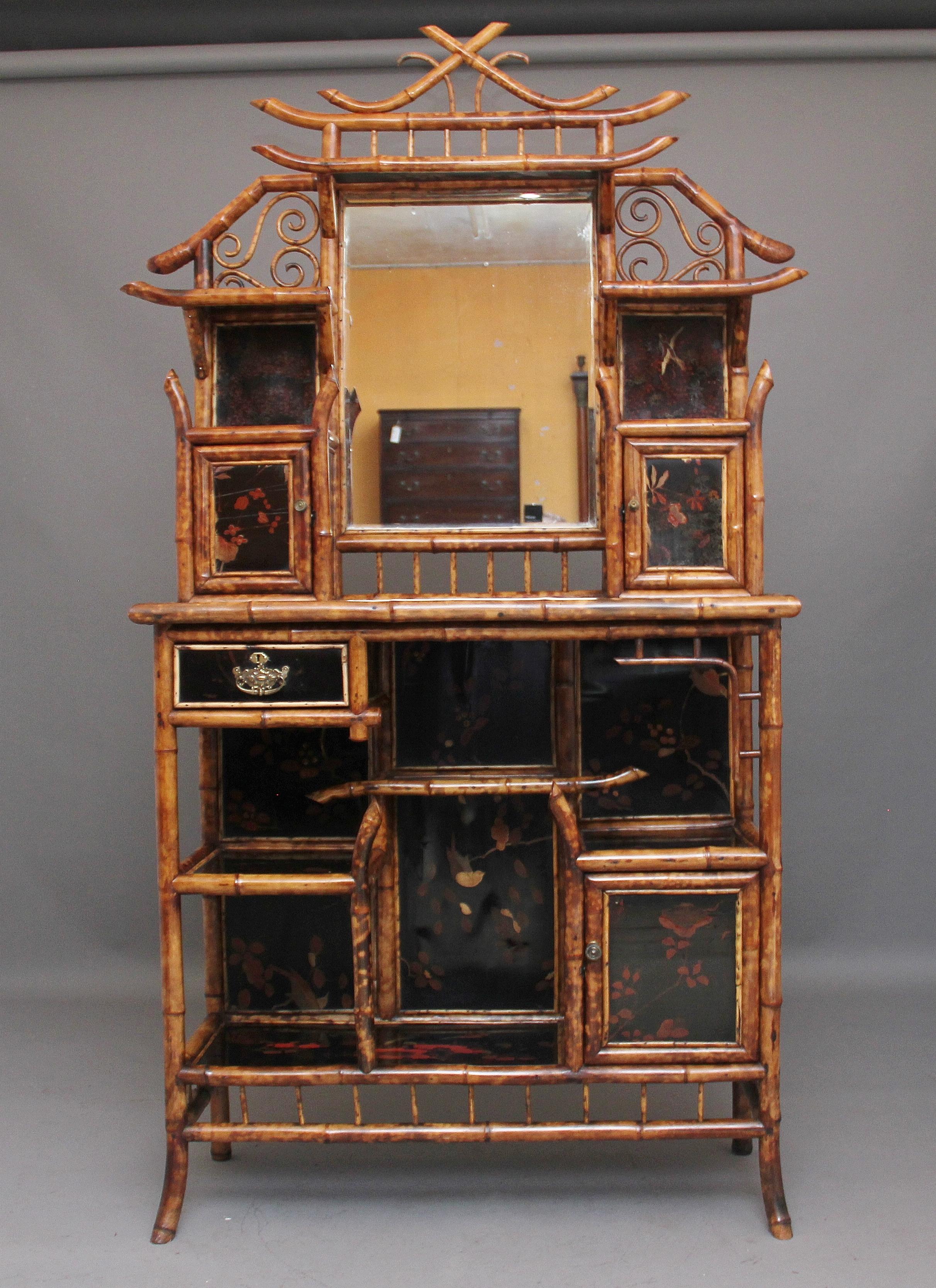 An impressive 19th century bamboo cabinet, having twenty nine original decorative lacquer panels depicting floral scenes, a mirrored shelved back, various cupboards and shelves and a drawer with brass plate handle, the shaped bamboo makes this