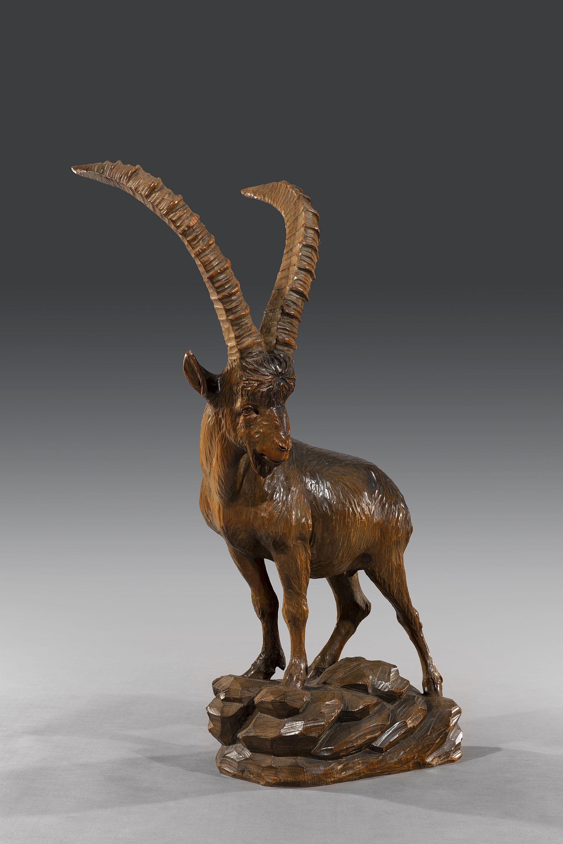 An imposing 'Black Forest' lime wood carving of an ibex standing on a rocky out-crop. The ibex is posed looking down a mountain and is expertly carved with excellent posture.