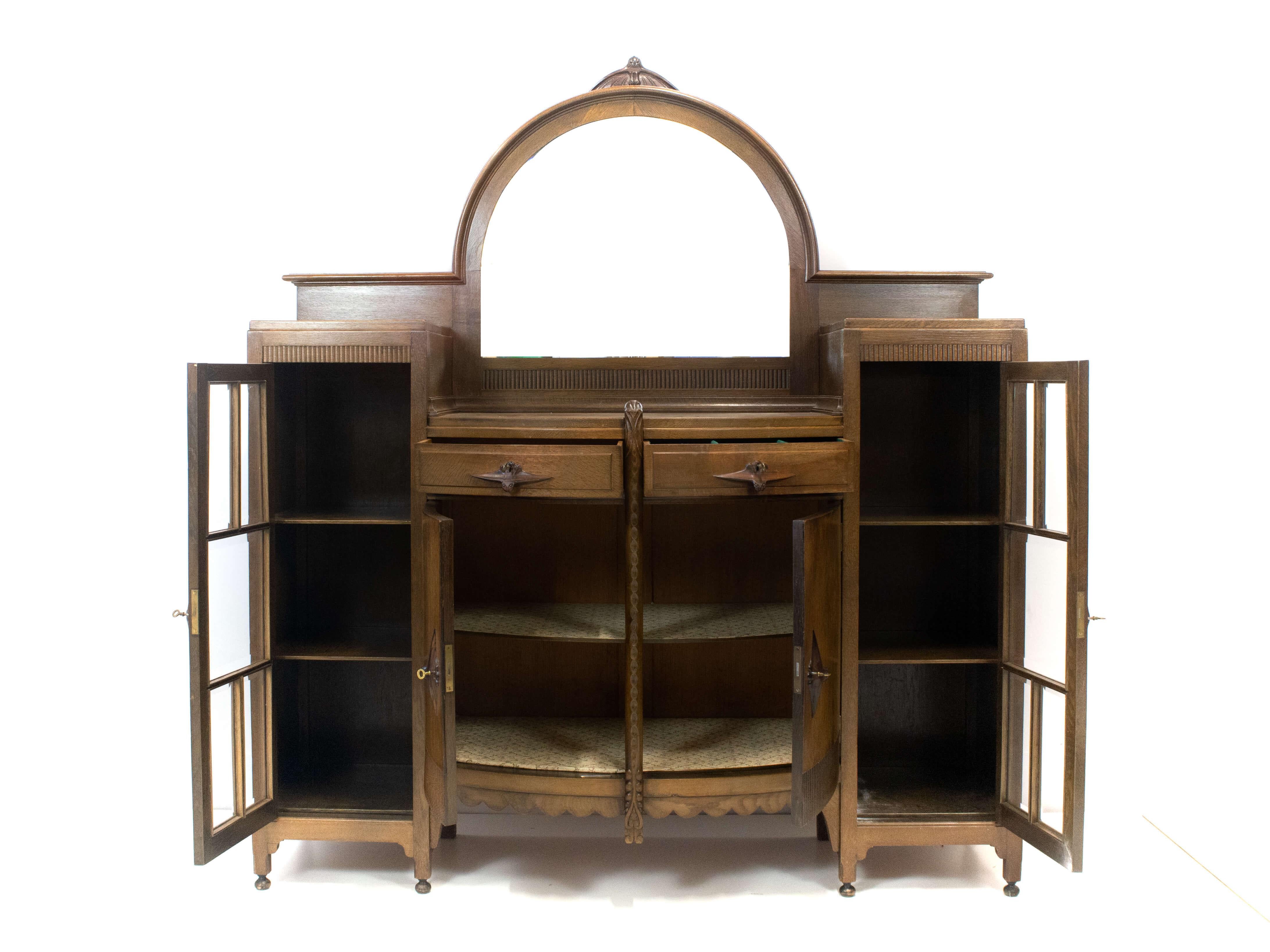 Impressive Amsterdam School bar cabinet by J.Th. Drilling, The Netherlands 1920s. This bar cabinet has two faceted glass doors, two round-shaped closed doors and two round-shaped drawers. On top of the cabinet is a large mirror with one small crack