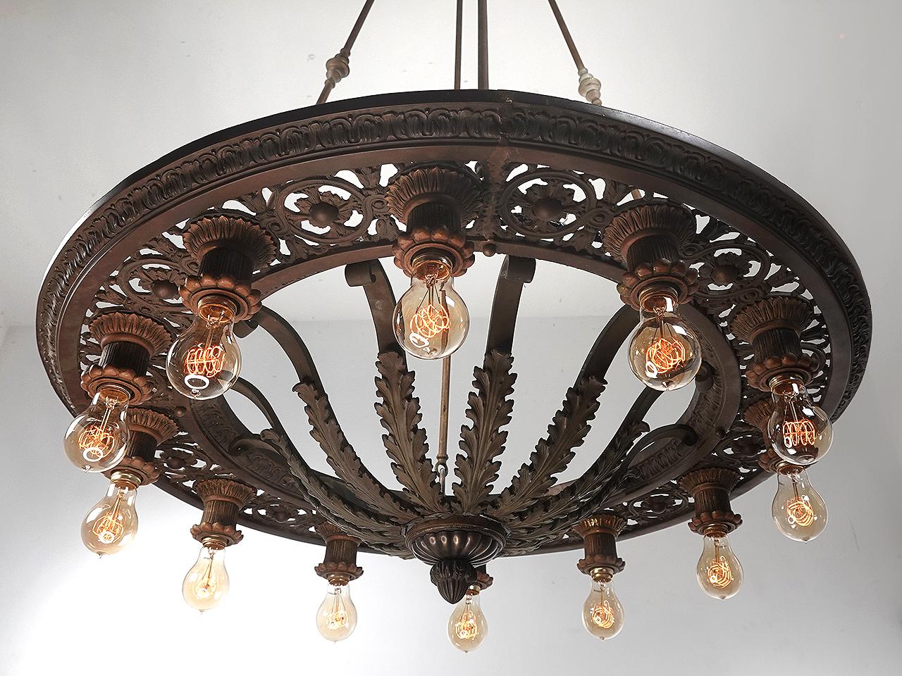 These are classic heavy cast bronze pierced acanthus leaf ring light theater chandeliers. Each industrial size lamp uses 12 bulbs. The detail of the castings are absolutely marvelous with pierced cast bronze ring and flowing decor, fluted socket