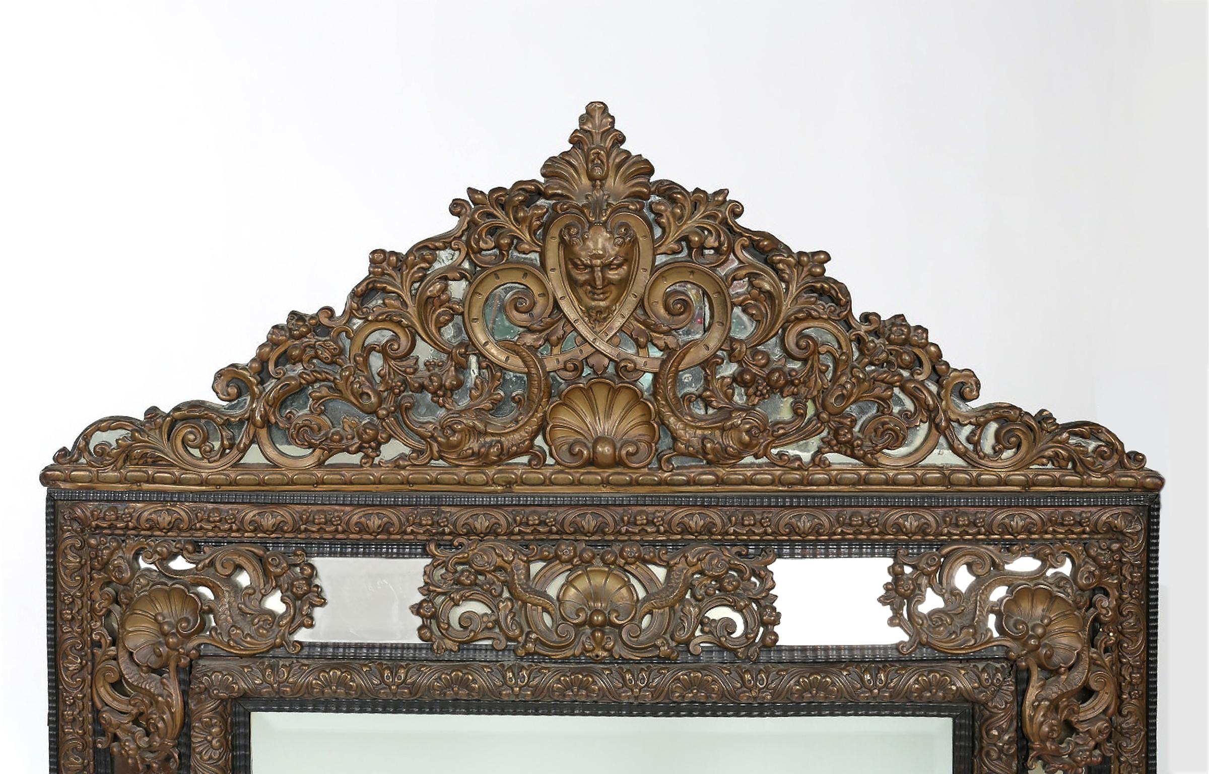 Impressive Baroque style with brass embossed beveled hanging wall mirror. The mirror is in good condition with wear appropriate to age / use. The mirror measure about 63 inches high x 40.5 inches wide.