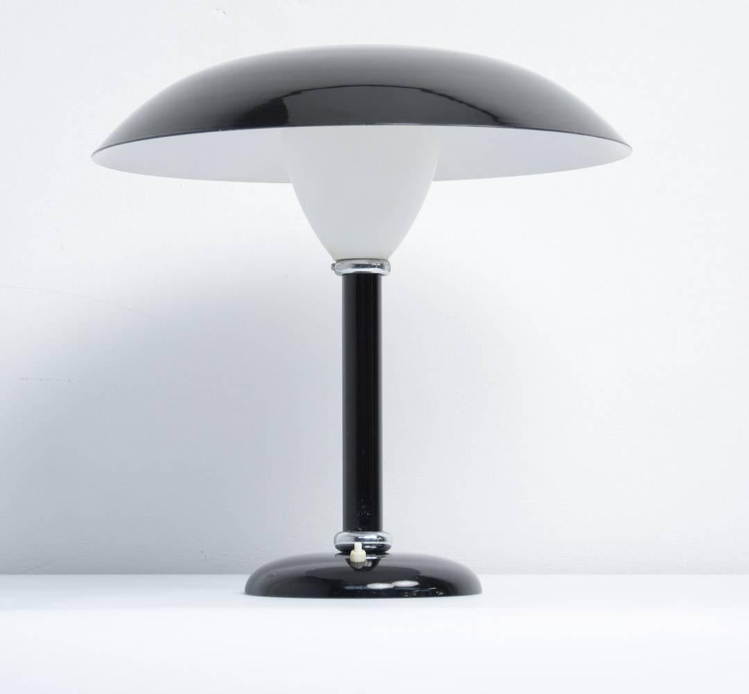 This large desk lamp can be dated in the 1930s and is made in the Bauhaus style.
Both the shade and the stem are made of black lacquered metal. The light diffuser in white frosted glass creates a pleasant light.
The lamp is finished with chrome