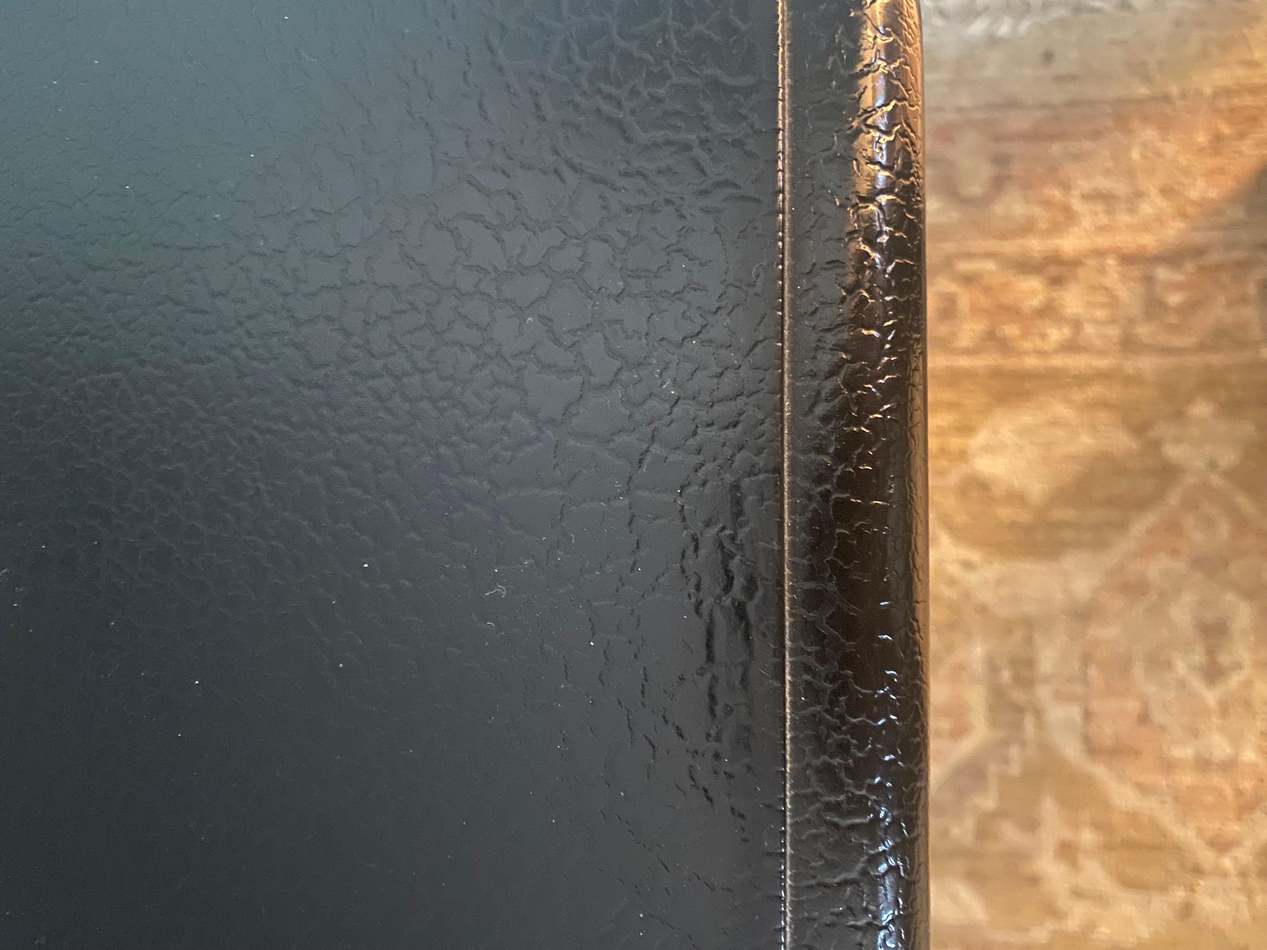 Elegante mesa de centro cuadrada de estilo Hollywood Regency en negro con detalles dorados que tiene lo que parece un tablero envuelto en piel.

MD