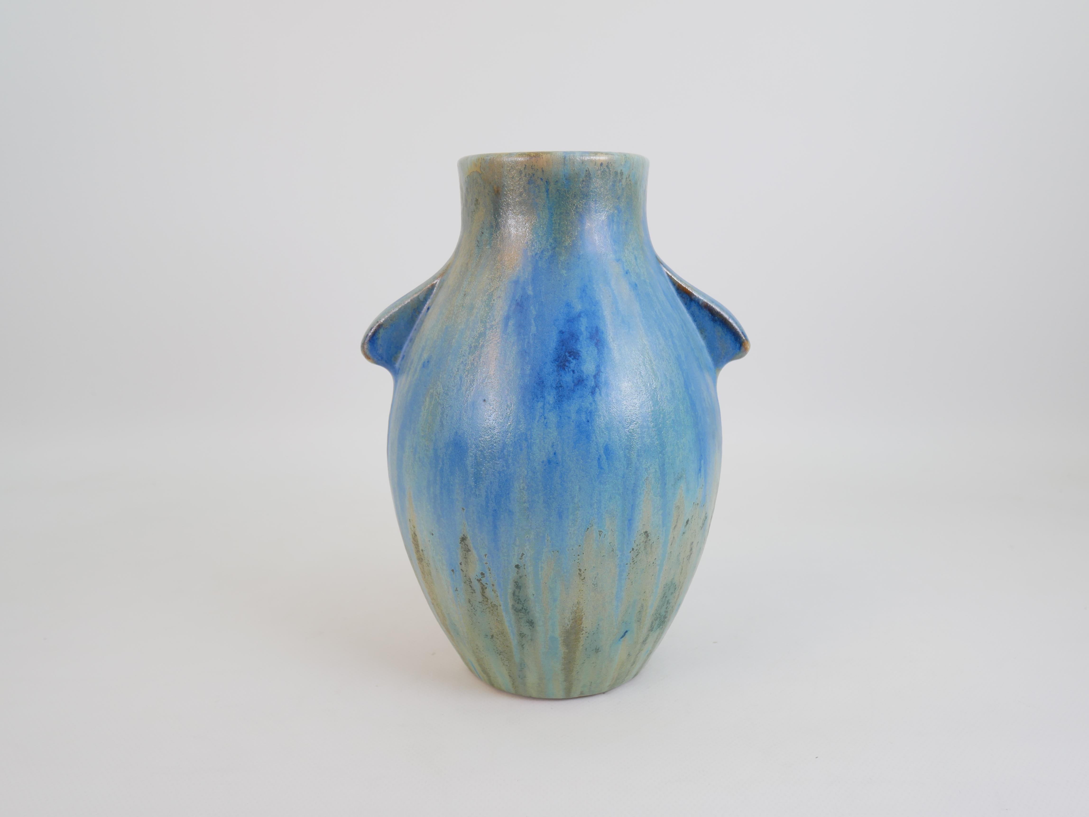 Ce vase en grès de la célèbre manufacture de Pierrefonds met en valeur la maîtrise des émaux flambés et cristallins, signature de la marque. Sa forme arrondie et organique est ponctuée par deux subtiles poignées en forme d'ailes qui émergent