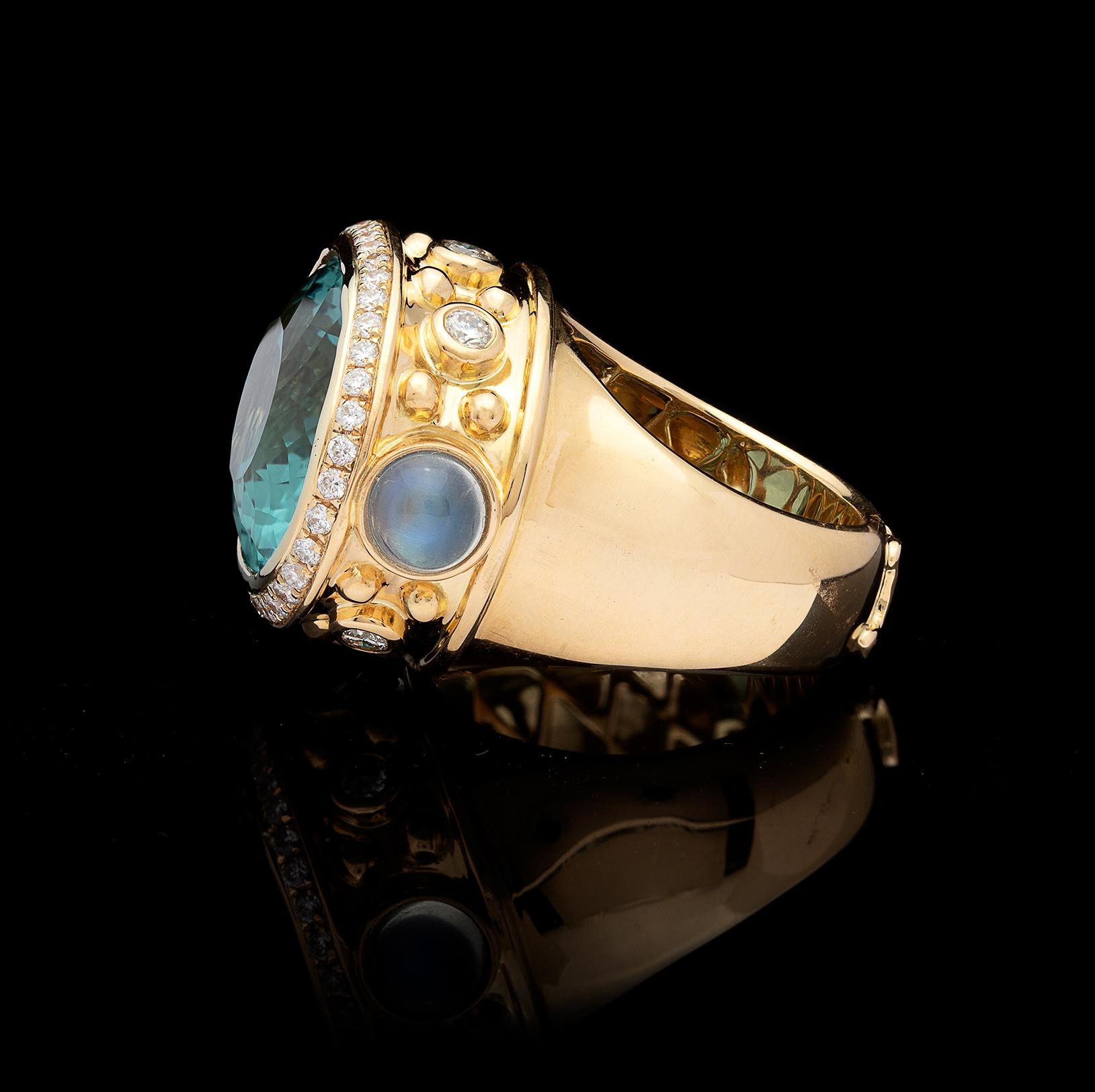 Boldly contemporary, this 18k yellow gold custom handmade ring is designed with a 17-ct. horizontally bezel-set teal blue topaz, with the surrounded frame accented by 2 cabochon moonstones and 42 round brilliant-cut diamonds. Total diamond weight