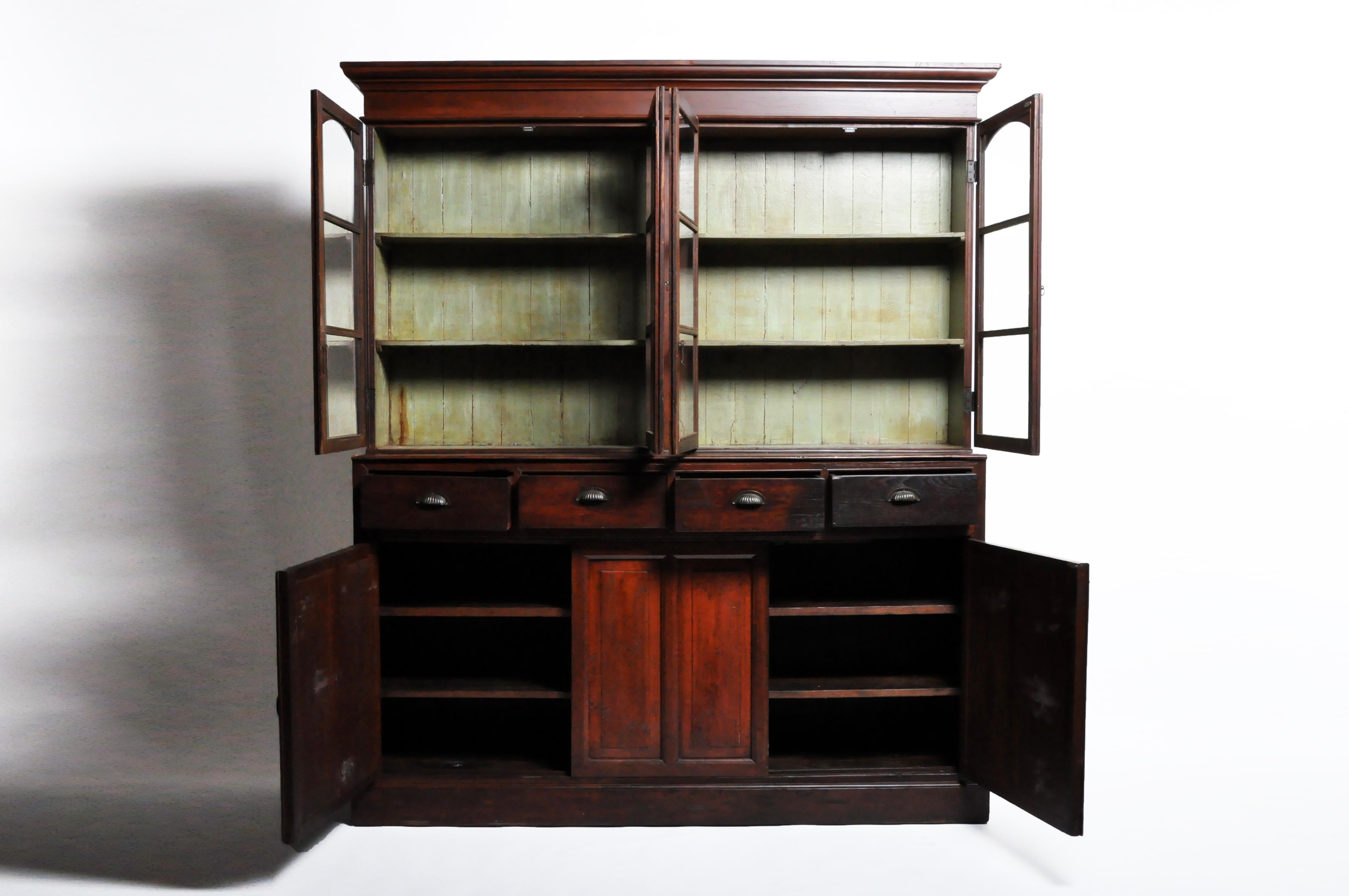 This handsome British Colonial cabinet comes in two parts, the top having 4 glass doors that open up to shelves for ample storage over another set of 3 doors with additional shelves, and 4 drawers for additional storage. Both open to compartments