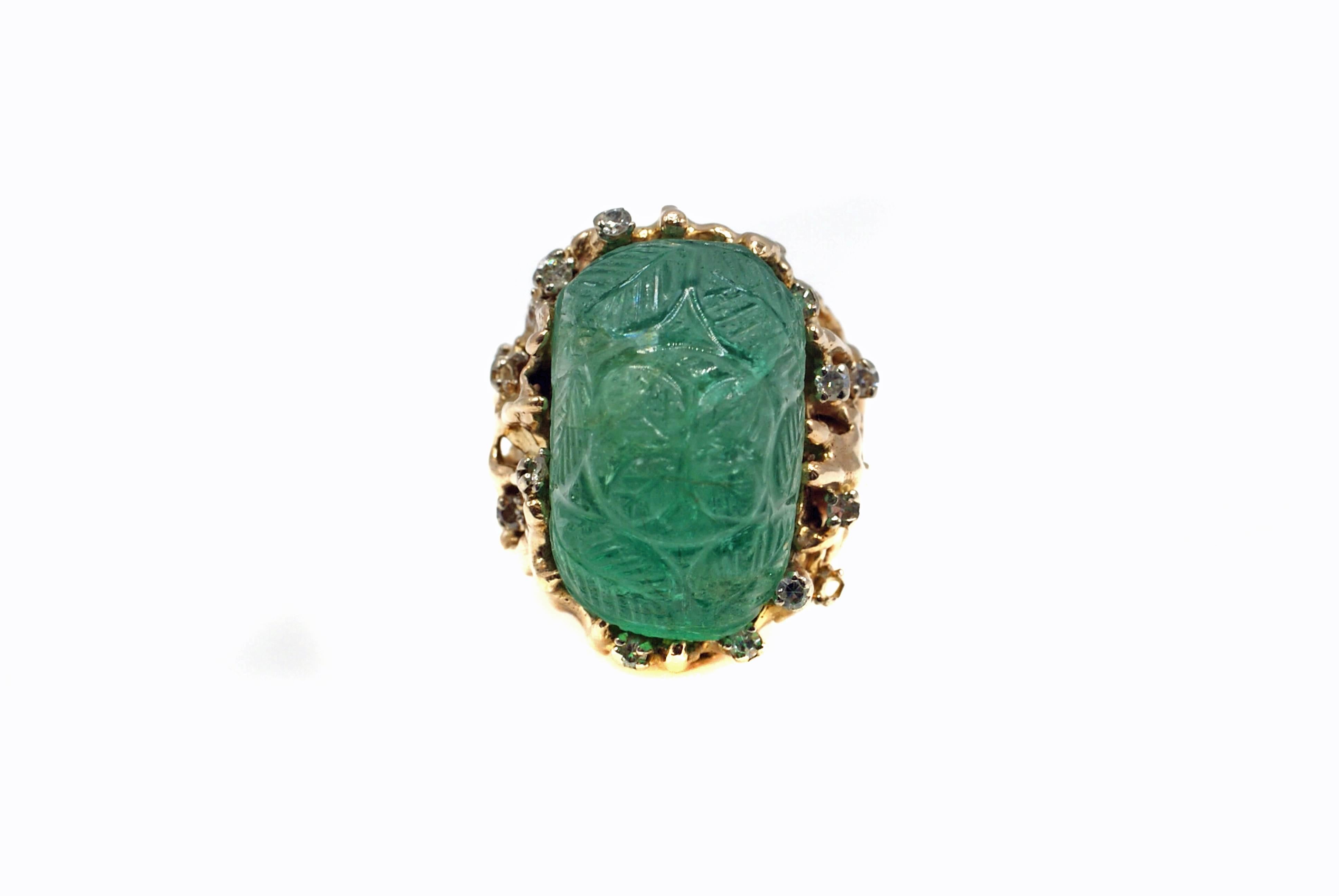 This intricately carved cabochon emerald measured to weigh approximately 40 carats is set in an abstract free-form 14 karat yellow mounting. The handcrafted ring mount is accented by 12 round brilliant cut diamonds and resembles a forest of trees